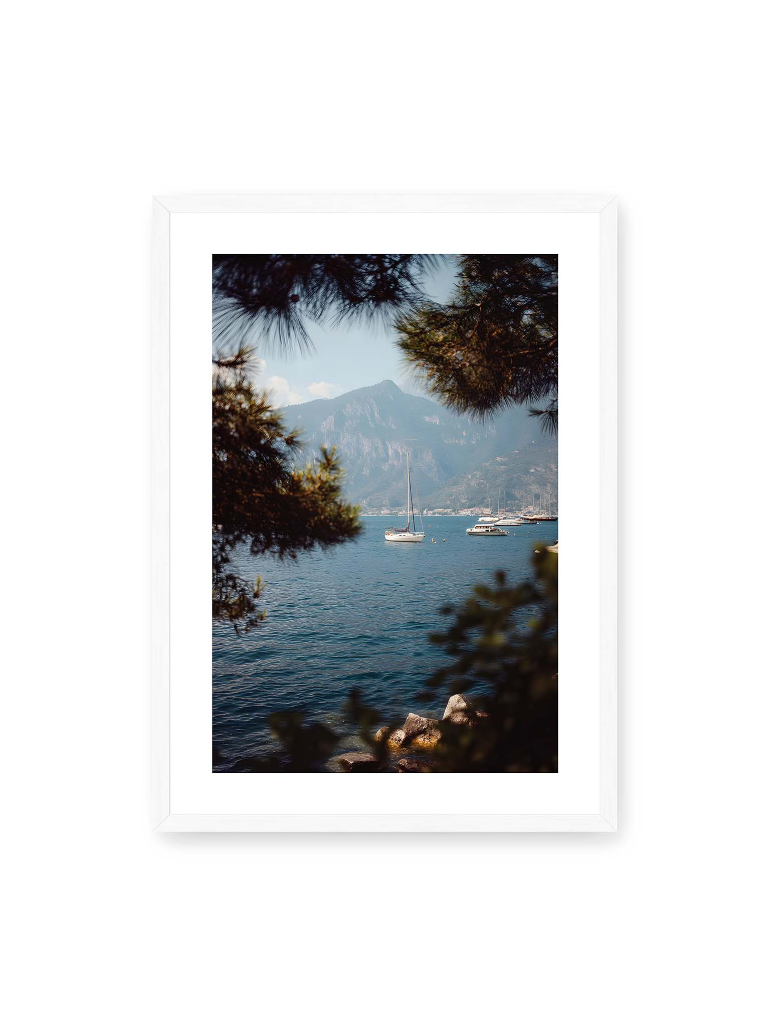 50x70 cm, weißer Galerie-Rand, weißer Rahmen – Segelboote im ruhigen Wasser vor Bergen, eingerahmt von unscharfen Ästen im Vordergrund.