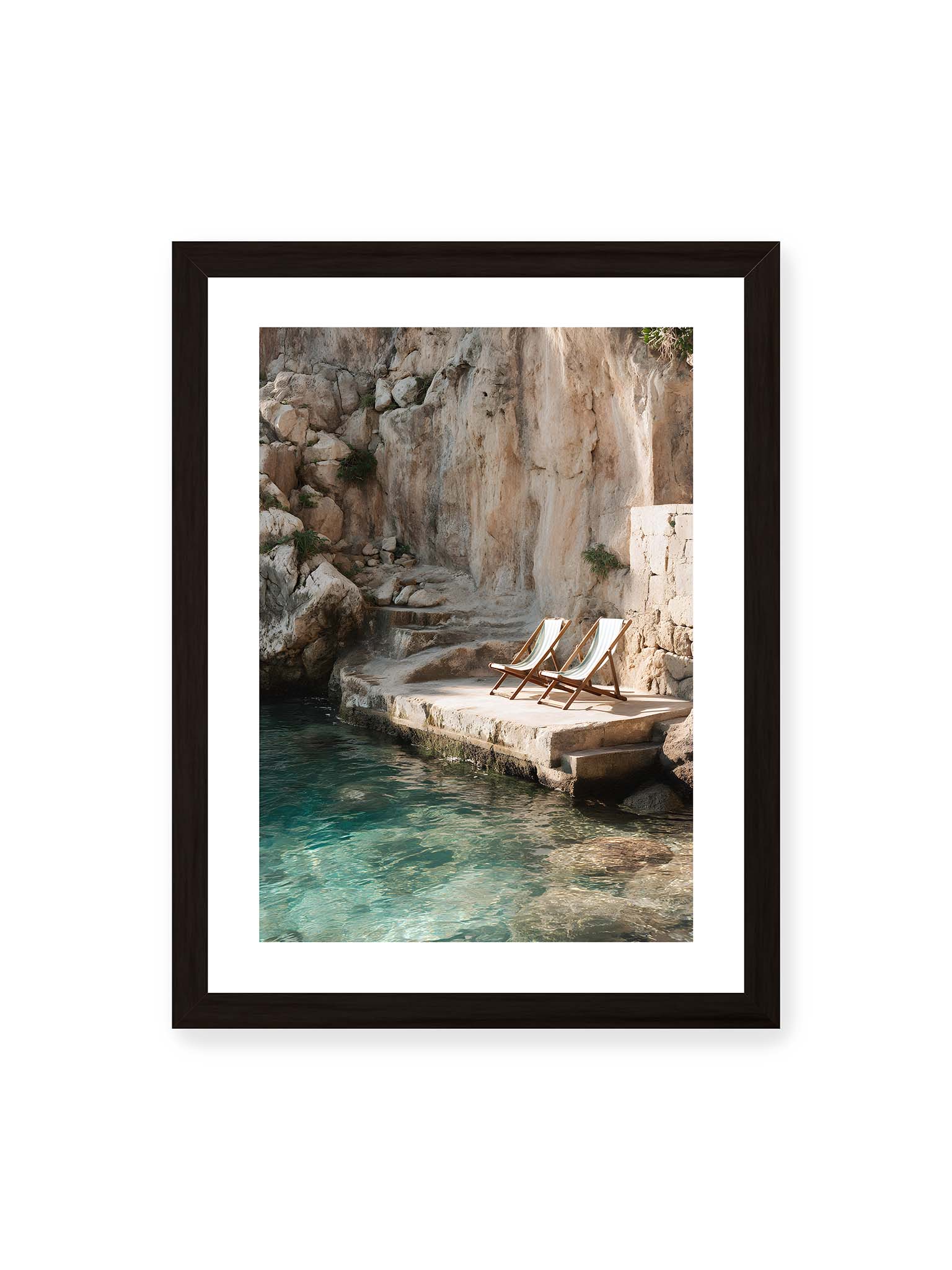 30x40 cm, weißer Galerie-Rand, schwarzer Rahmen – Zwei Liegestühle auf Felsplattform am klaren Wasser, umgeben von rauer Küstenwand und sanftem Licht.