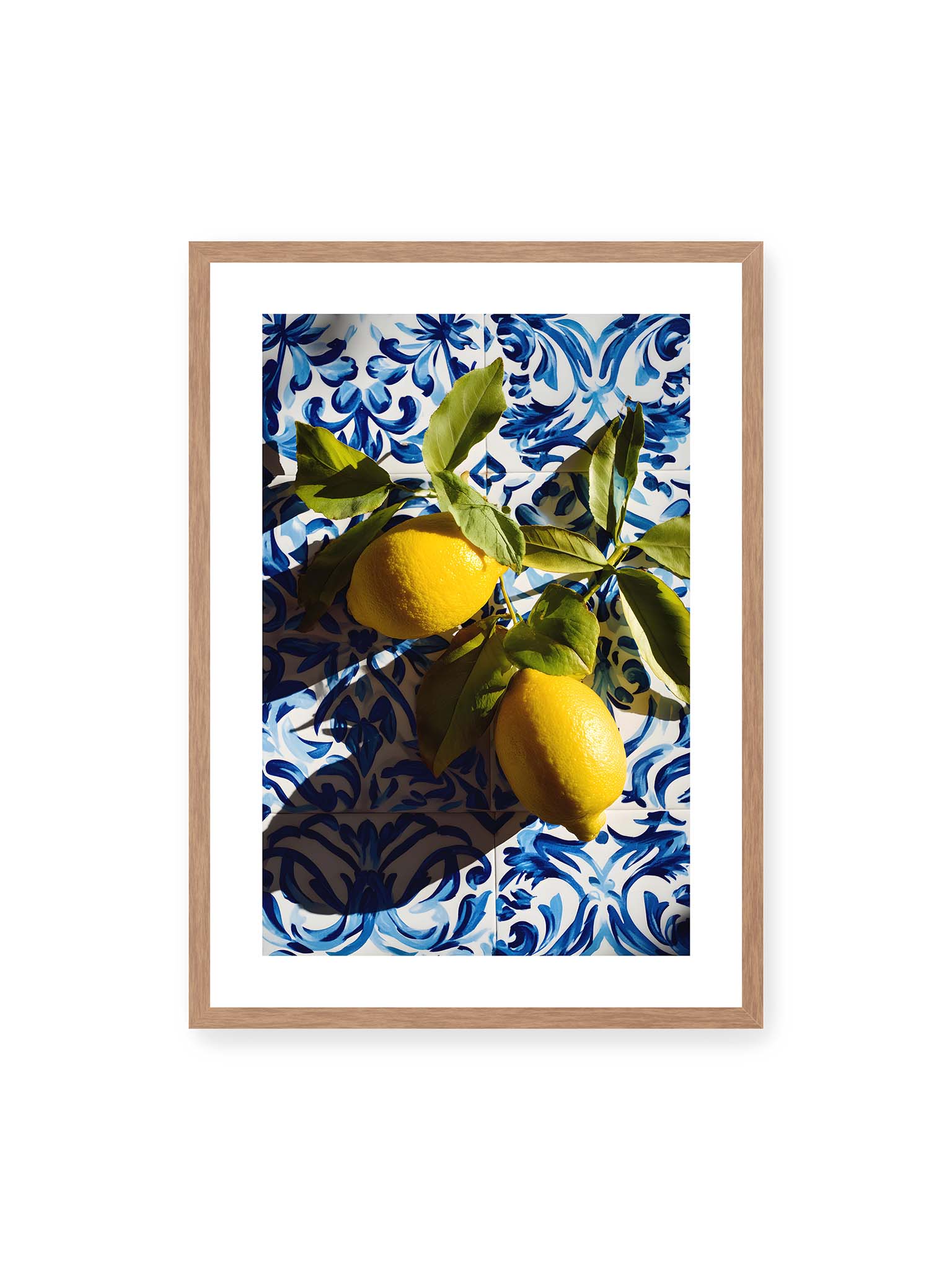 50x70 cm, weißer Galerie-Rand, Eichenrahmen – Zitronen mit Blättern auf blau gemusterten Fliesen mit starkem Licht und klaren Schatten.