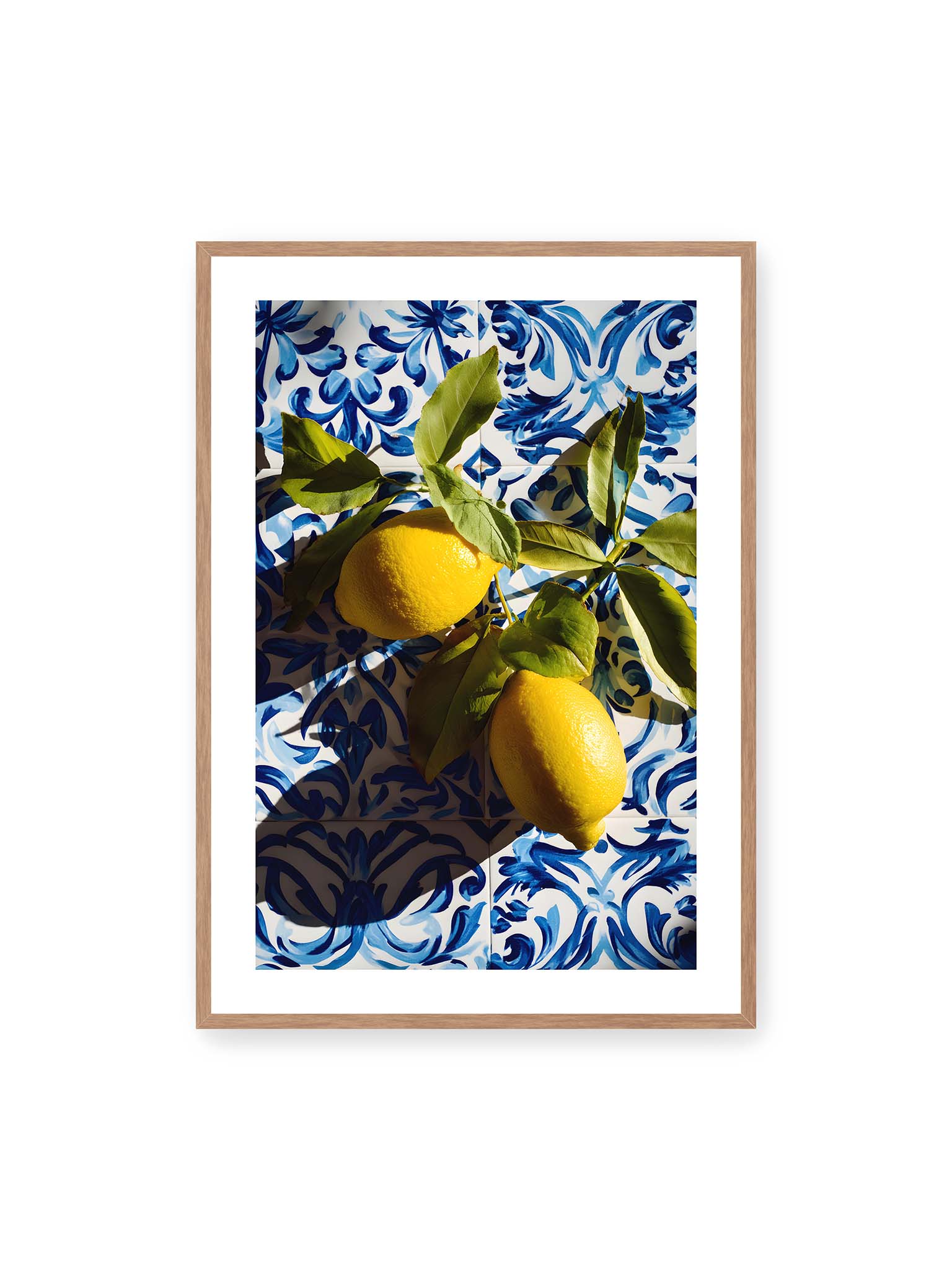 70x100 cm, weißer Galerie-Rand, Eichenrahmen – Zitronen mit Blättern auf blau gemusterten Fliesen mit starkem Licht und klaren Schatten.