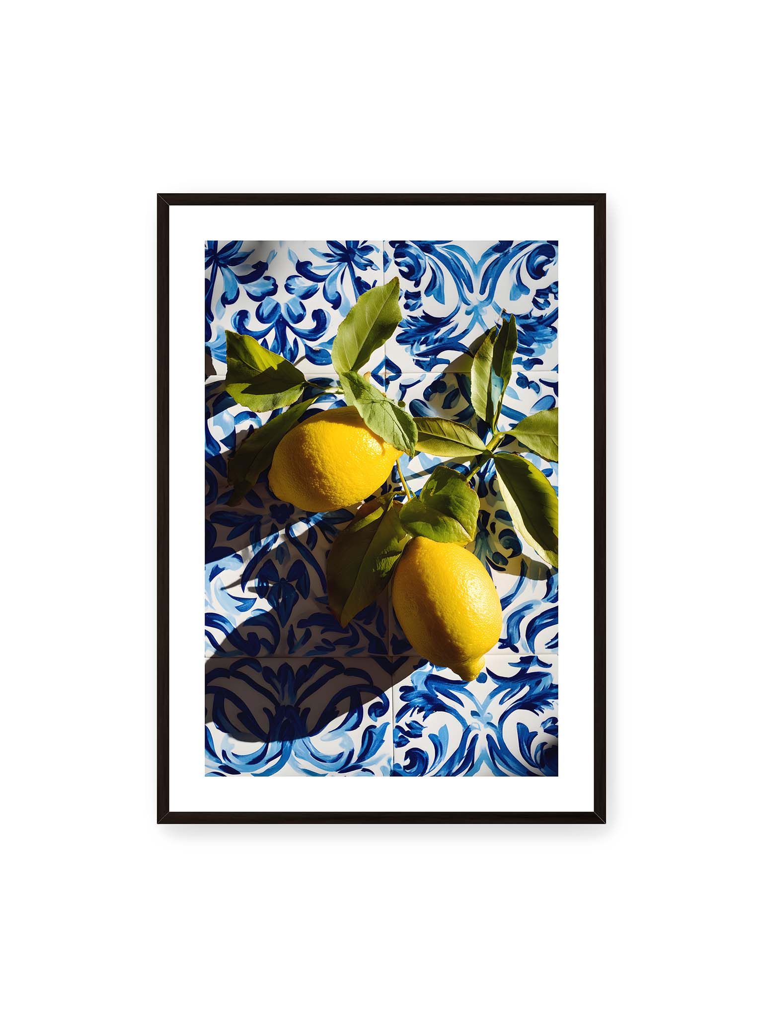 70x100 cm, weißer Galerie-Rand, schwarzer Rahmen – Zitronen mit Blättern auf blau gemusterten Fliesen mit starkem Licht und klaren Schatten.