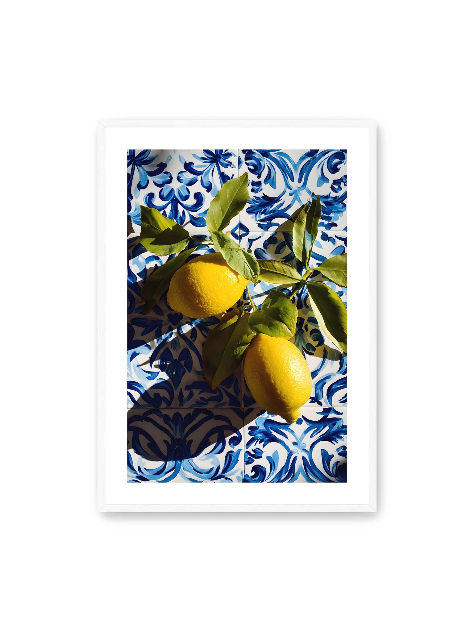 70x100 cm, weißer Galerie-Rand, weißer Rahmen – Zitronen mit Blättern auf blau gemusterten Fliesen mit starkem Licht und klaren Schatten.