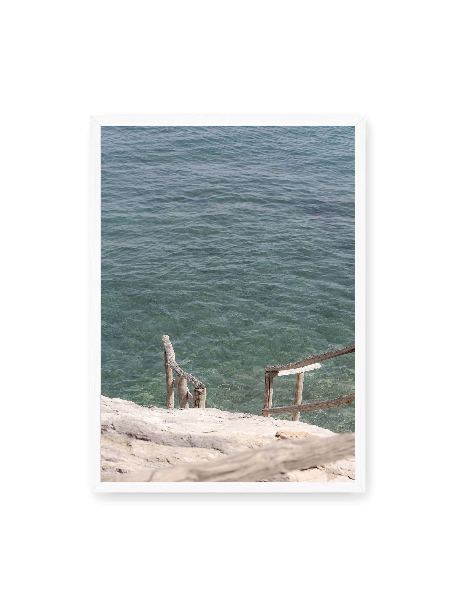 50x70 cm, weißer Rahmen – Holztreppe führt über helle Felsen in klares, ruhiges Meer mit sichtbarer Wasserstruktur.