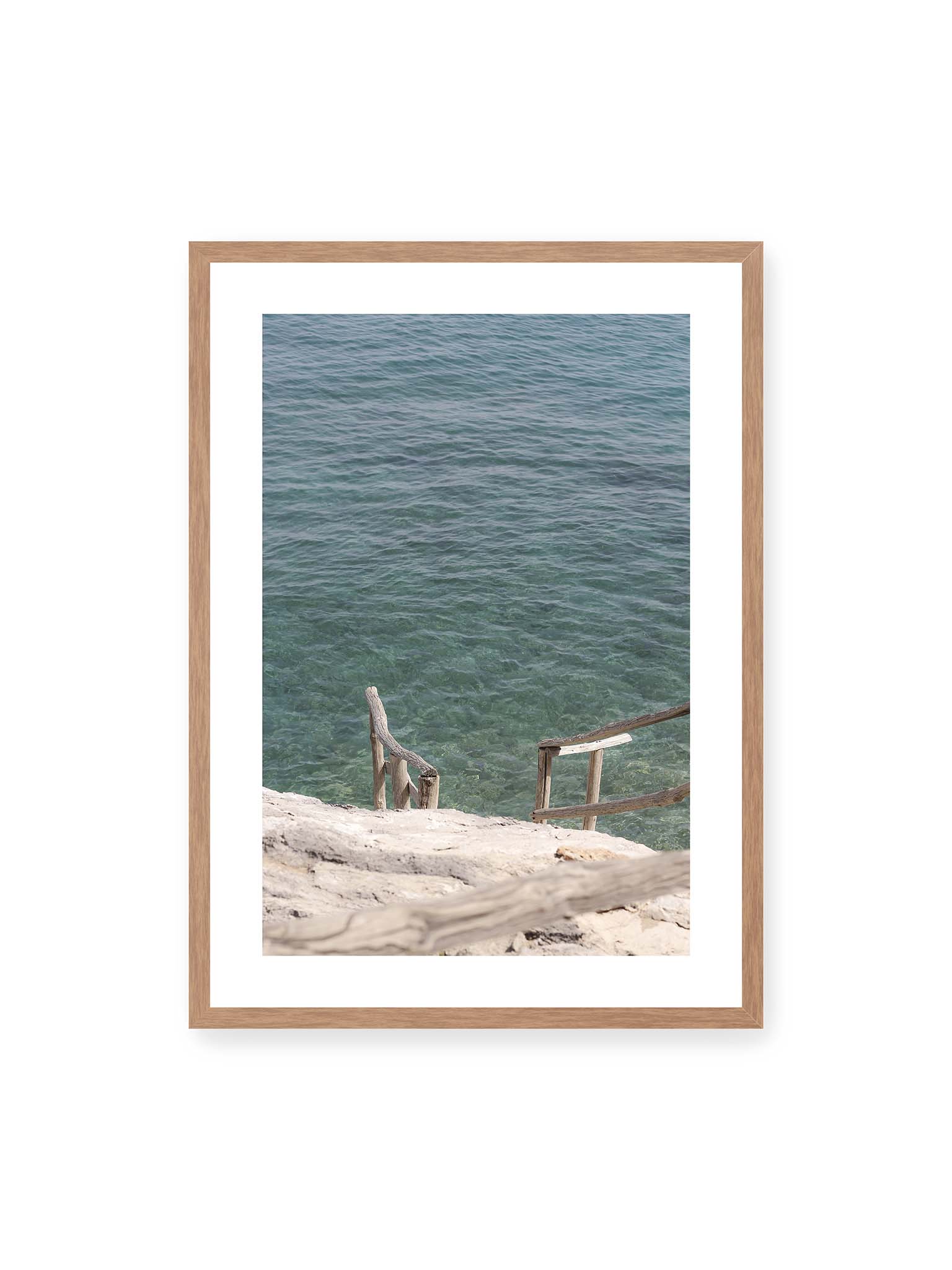 50x70 cm, weißer Galerie-Rand, Eichenrahmen – Holztreppe führt über helle Felsen in klares, ruhiges Meer mit sichtbarer Wasserstruktur.