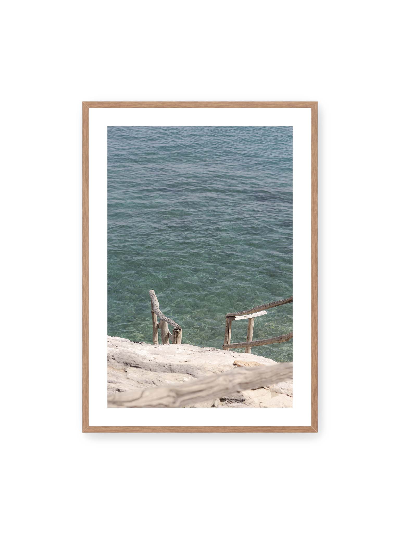 70x100 cm, weißer Galerie-Rand, Eichenrahmen – Holztreppe führt über helle Felsen in klares, ruhiges Meer mit sichtbarer Wasserstruktur.