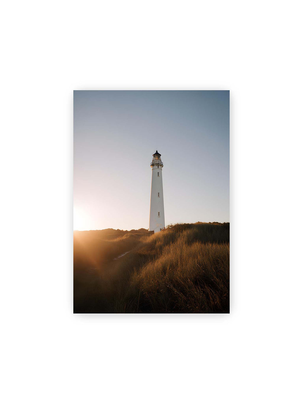 21x30 cm – Weißer Leuchtturm über Dünen im warmen Abendlicht mit sanftem Himmel im Hintergrund.