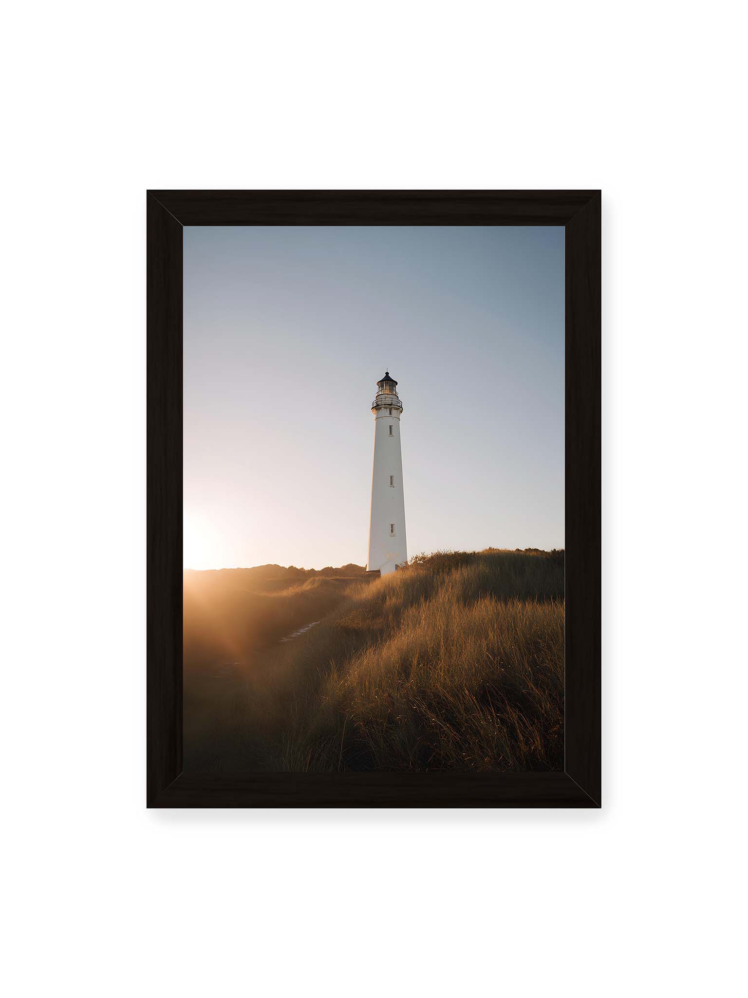 21x30 cm, schwarzer Rahmen – Weißer Leuchtturm über Dünen im warmen Abendlicht mit sanftem Himmel im Hintergrund.