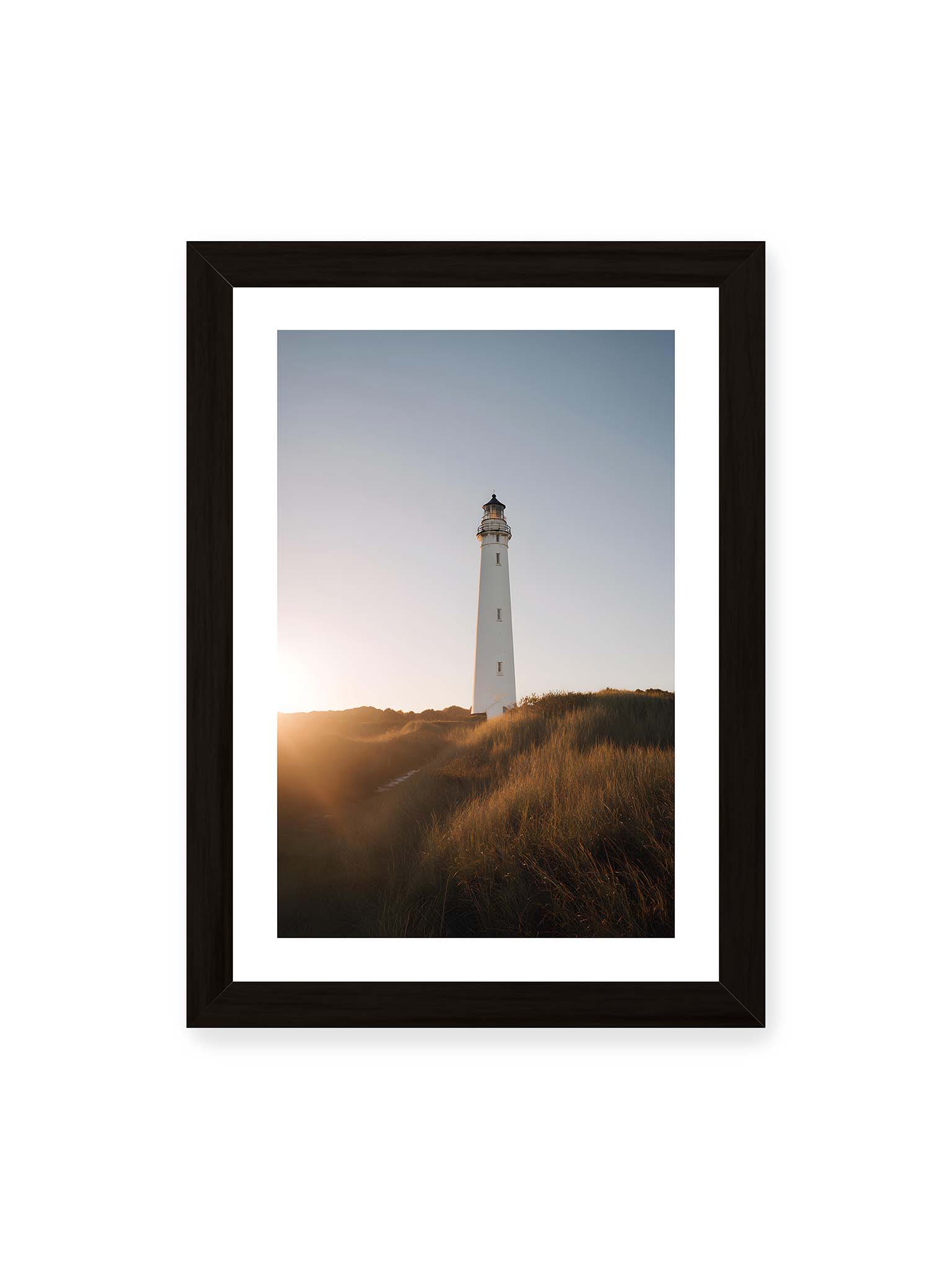 21x30 cm, weißer Galerie-Rand, schwarzer Rahmen – Weißer Leuchtturm über Dünen im warmen Abendlicht mit sanftem Himmel im Hintergrund.