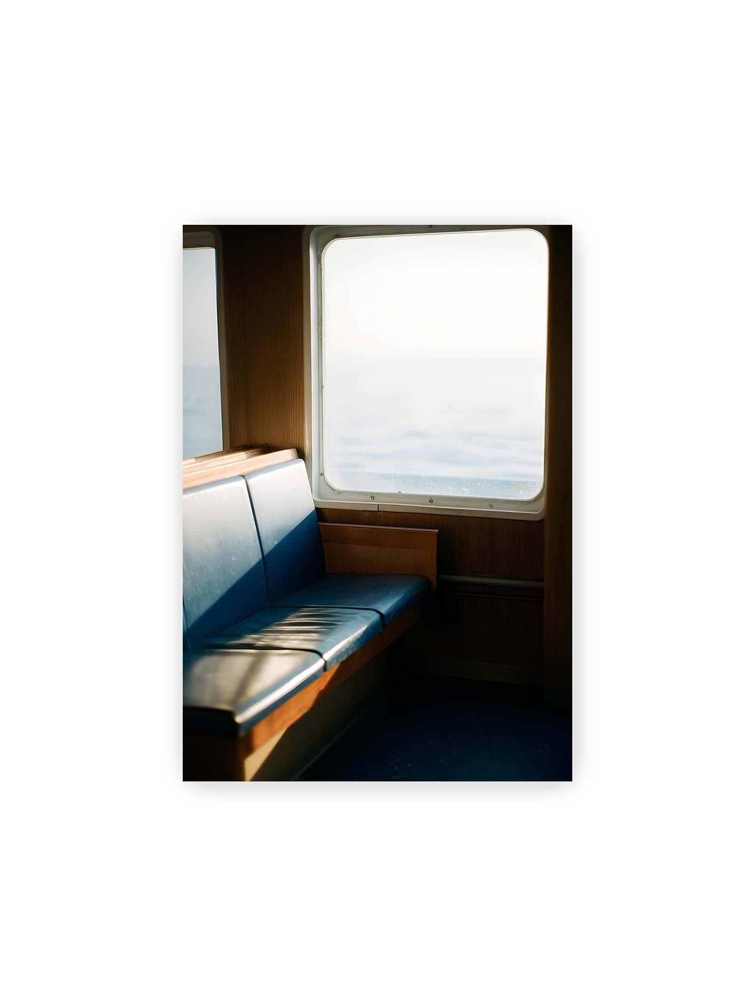 21x30 cm – Leerer Sitzplatz neben einem Fenster mit warmem Licht und unscharfer Aussicht auf das offene Meer.