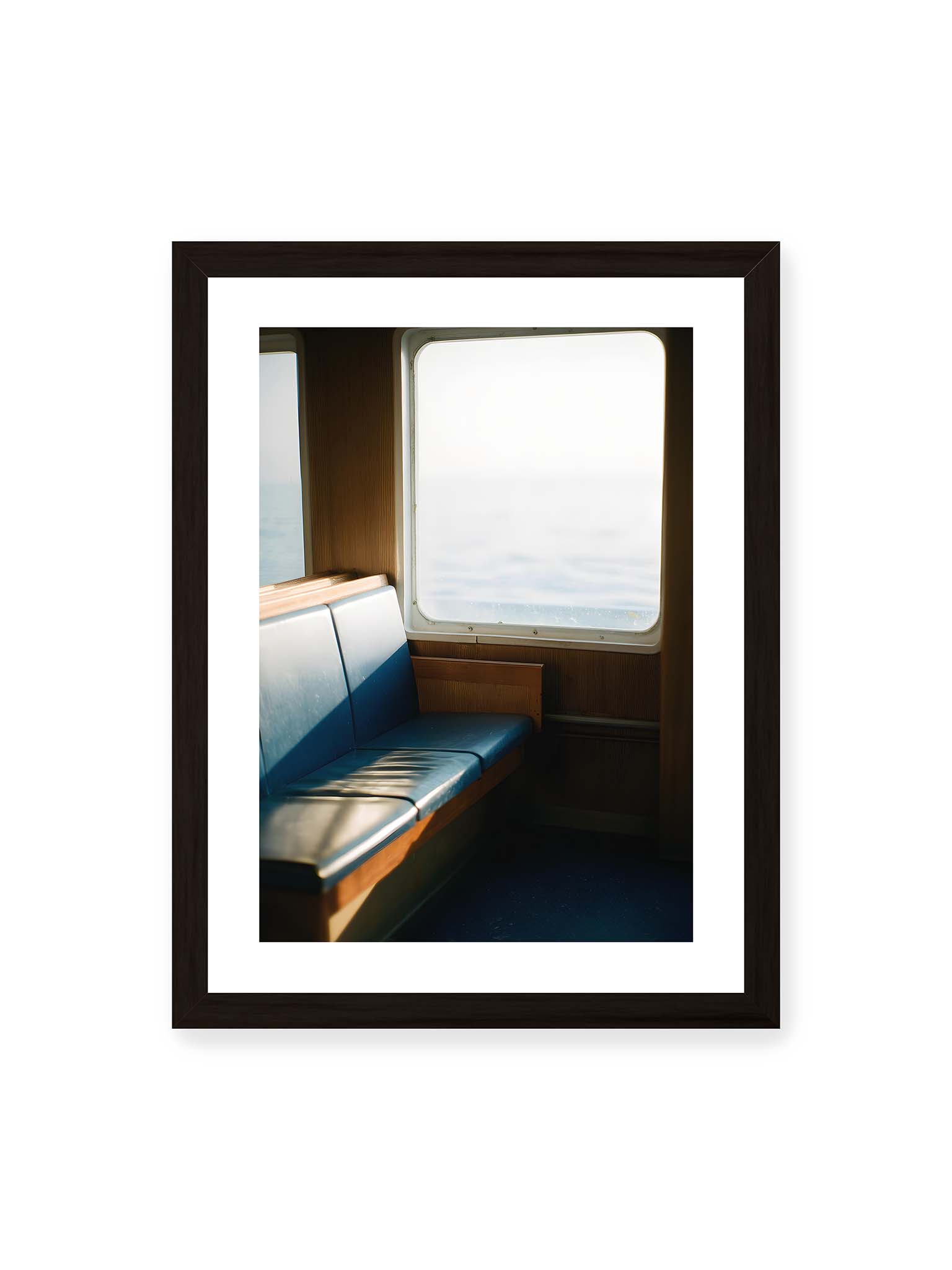 30x40 cm, weißer Galerie-Rand, schwarzer Rahmen – Leerer Sitzplatz neben einem Fenster mit warmem Licht und unscharfer Aussicht auf das offene Meer.
