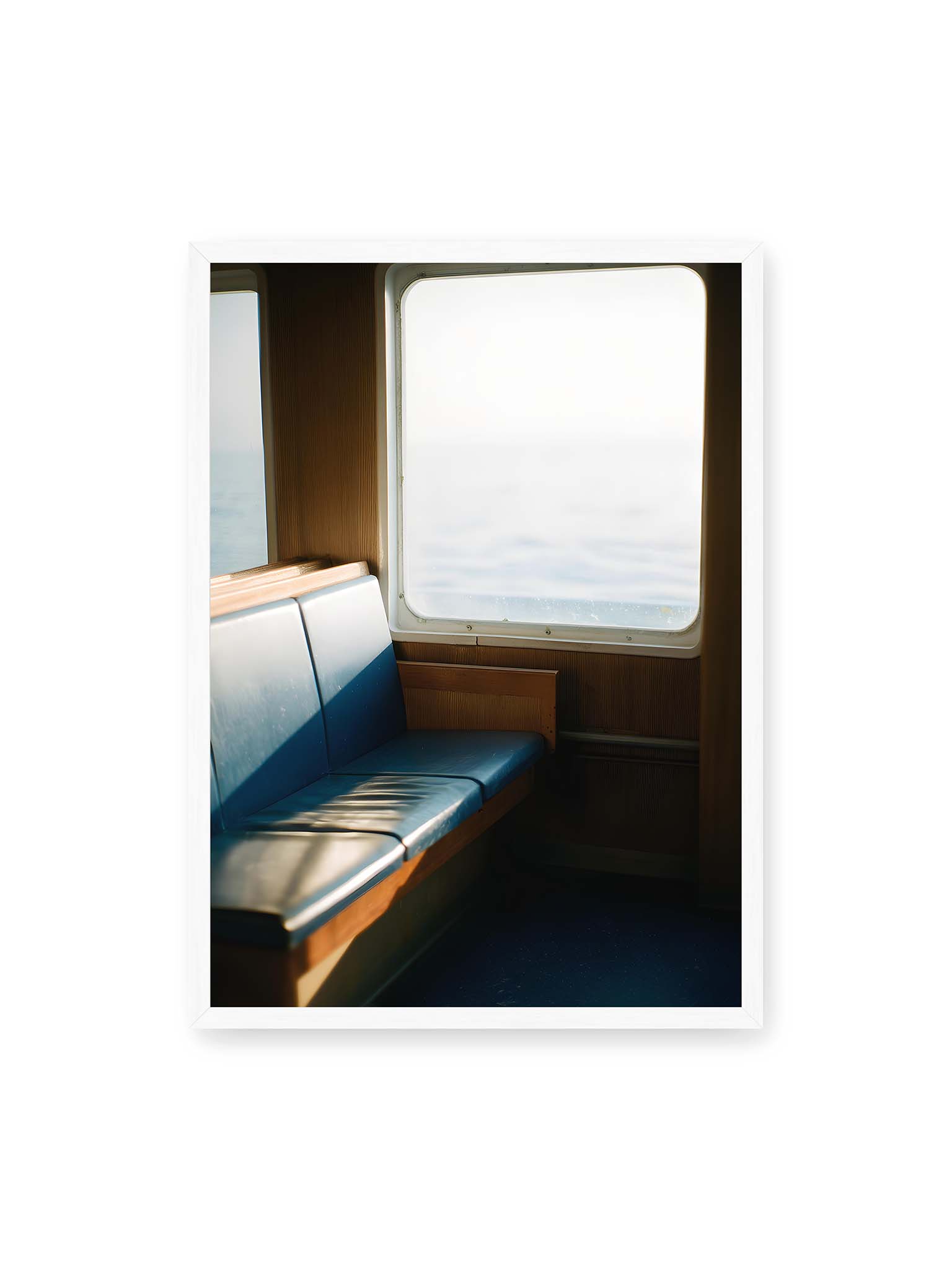 50x70 cm, weißer Rahmen – Leerer Sitzplatz neben einem Fenster mit warmem Licht und unscharfer Aussicht auf das offene Meer.