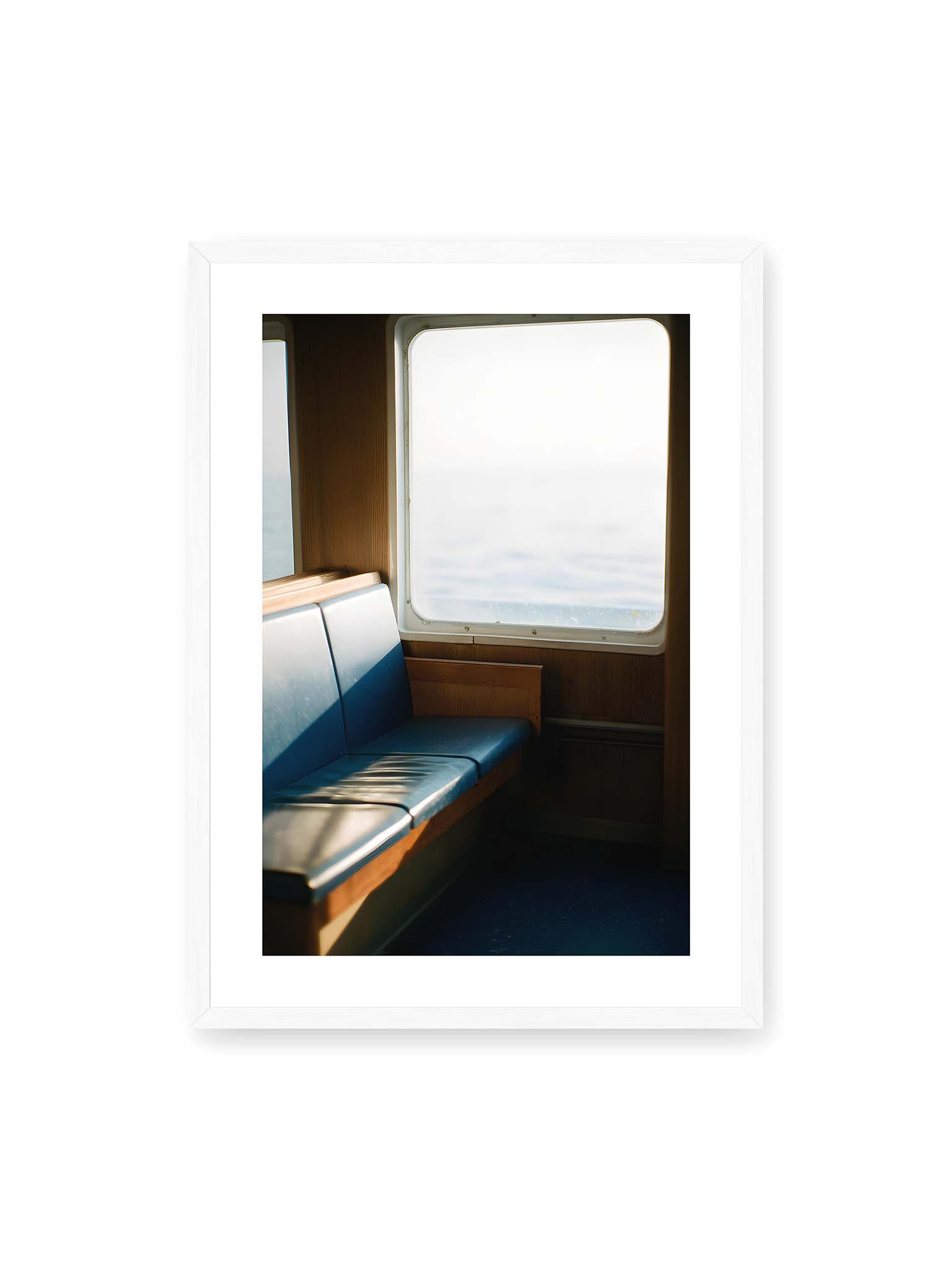 50x70 cm, weißer Galerie-Rand, weißer Rahmen – Leerer Sitzplatz neben einem Fenster mit warmem Licht und unscharfer Aussicht auf das offene Meer.
