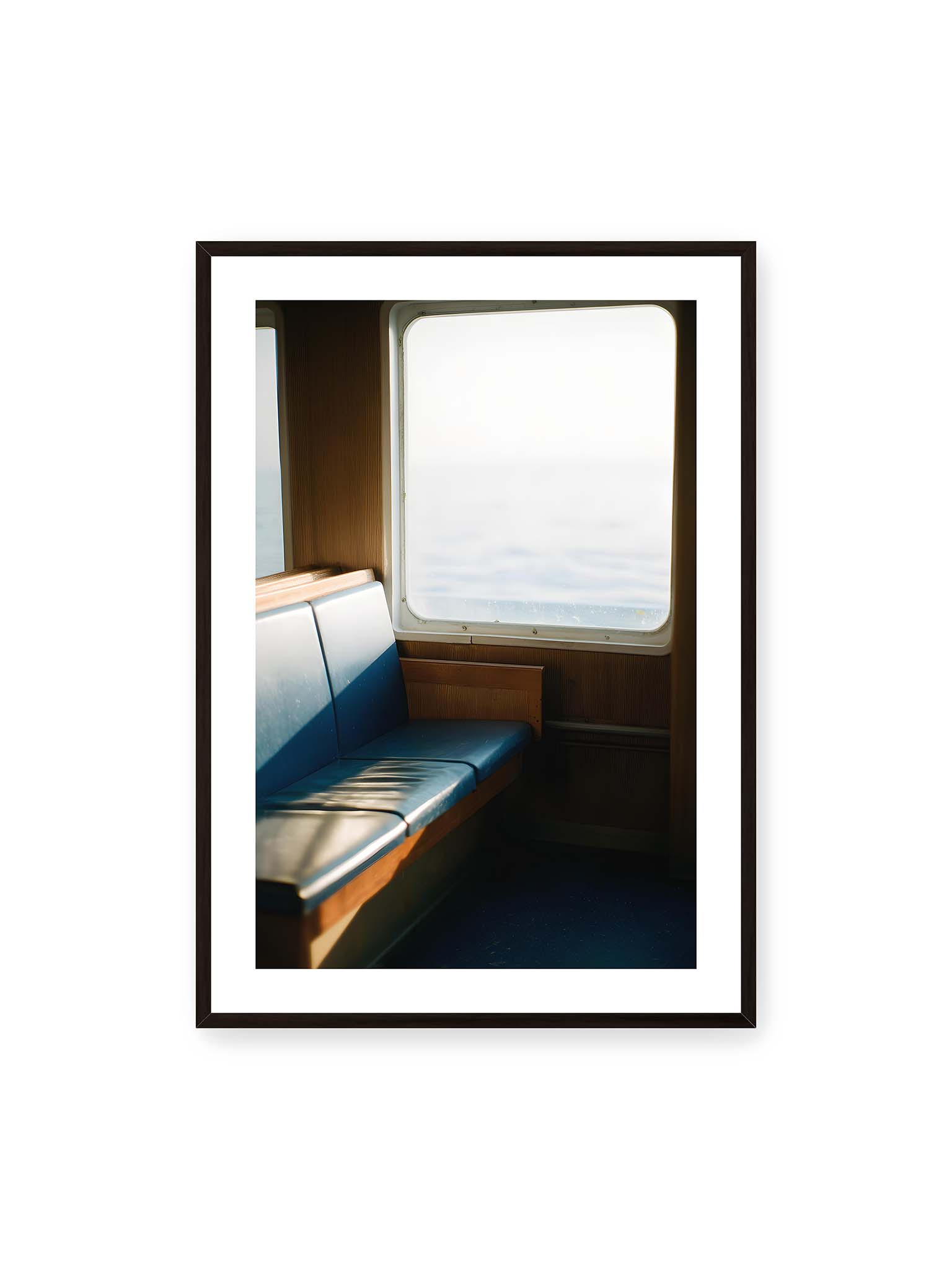 70x100 cm, weißer Galerie-Rand, schwarzer Rahmen – Leerer Sitzplatz neben einem Fenster mit warmem Licht und unscharfer Aussicht auf das offene Meer.