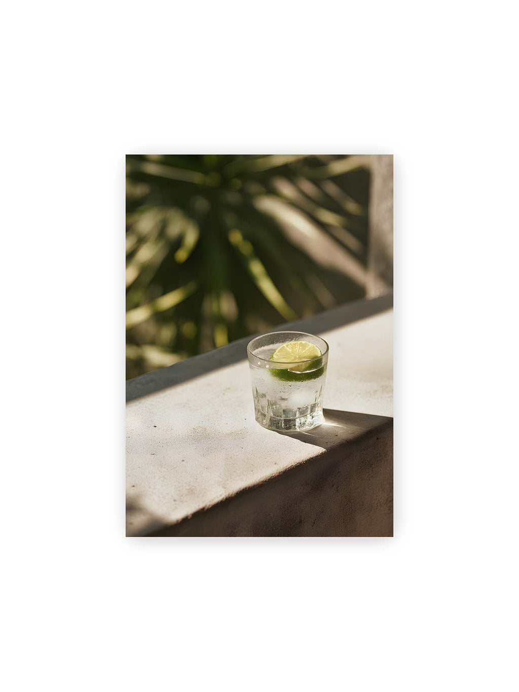 21x30 cm – Glas mit Eis und Limettenscheibe auf heller Oberfläche im warmen Licht mit tropischen Schatten.