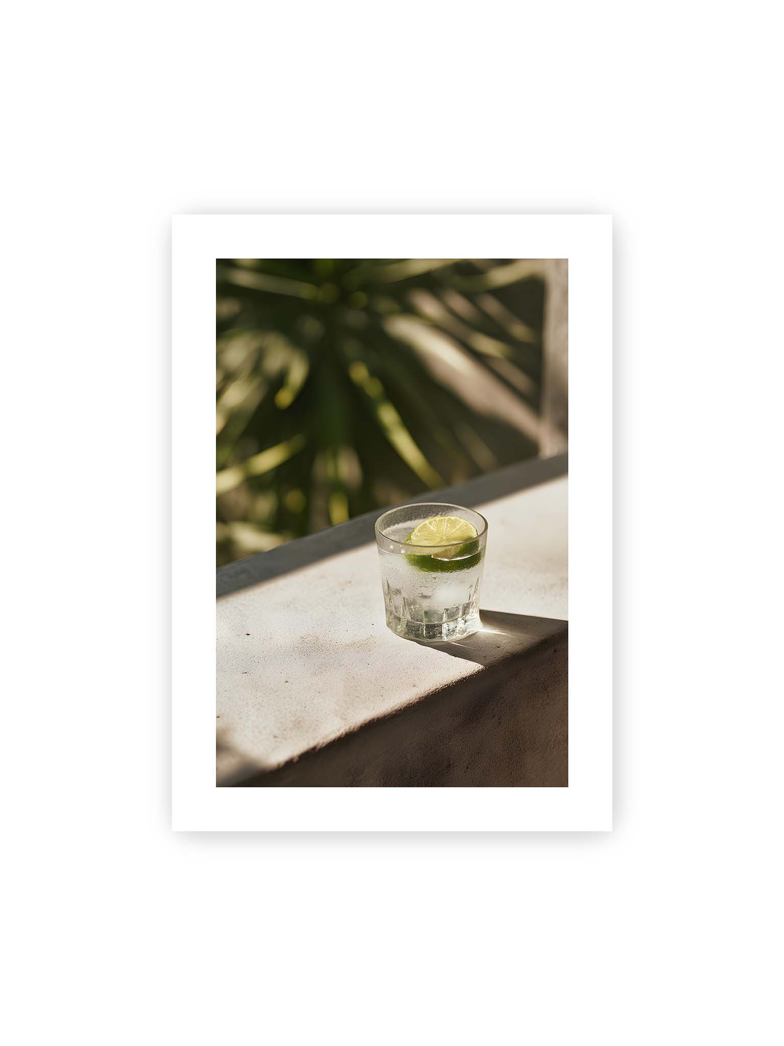 50x70 cm, weißer Galerie-Rand – Glas mit Eis und Limettenscheibe auf heller Oberfläche im warmen Licht mit tropischen Schatten.
