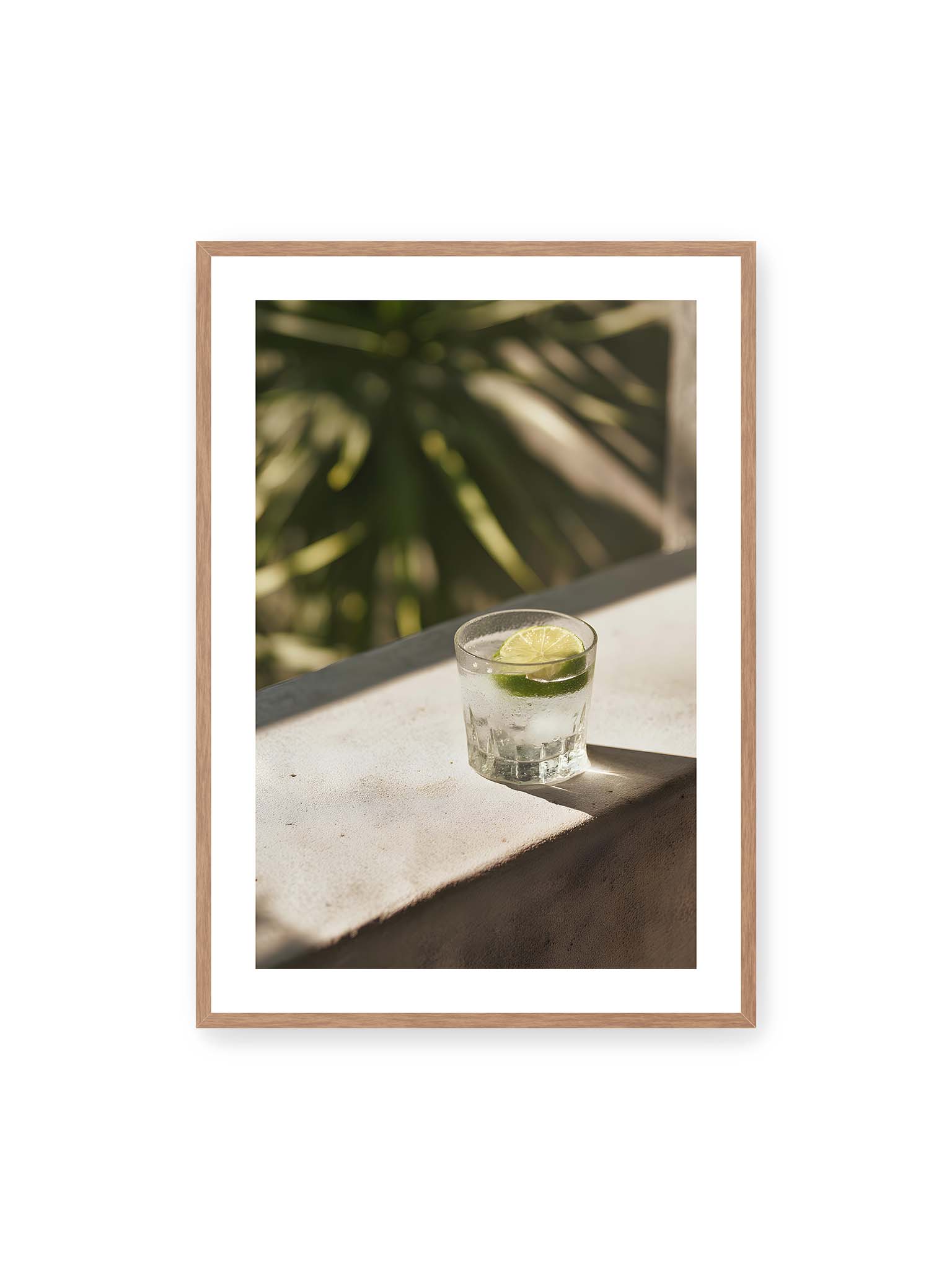 70x100 cm, weißer Galerie-Rand, Eichenrahmen – Glas mit Eis und Limettenscheibe auf heller Oberfläche im warmen Licht mit tropischen Schatten.