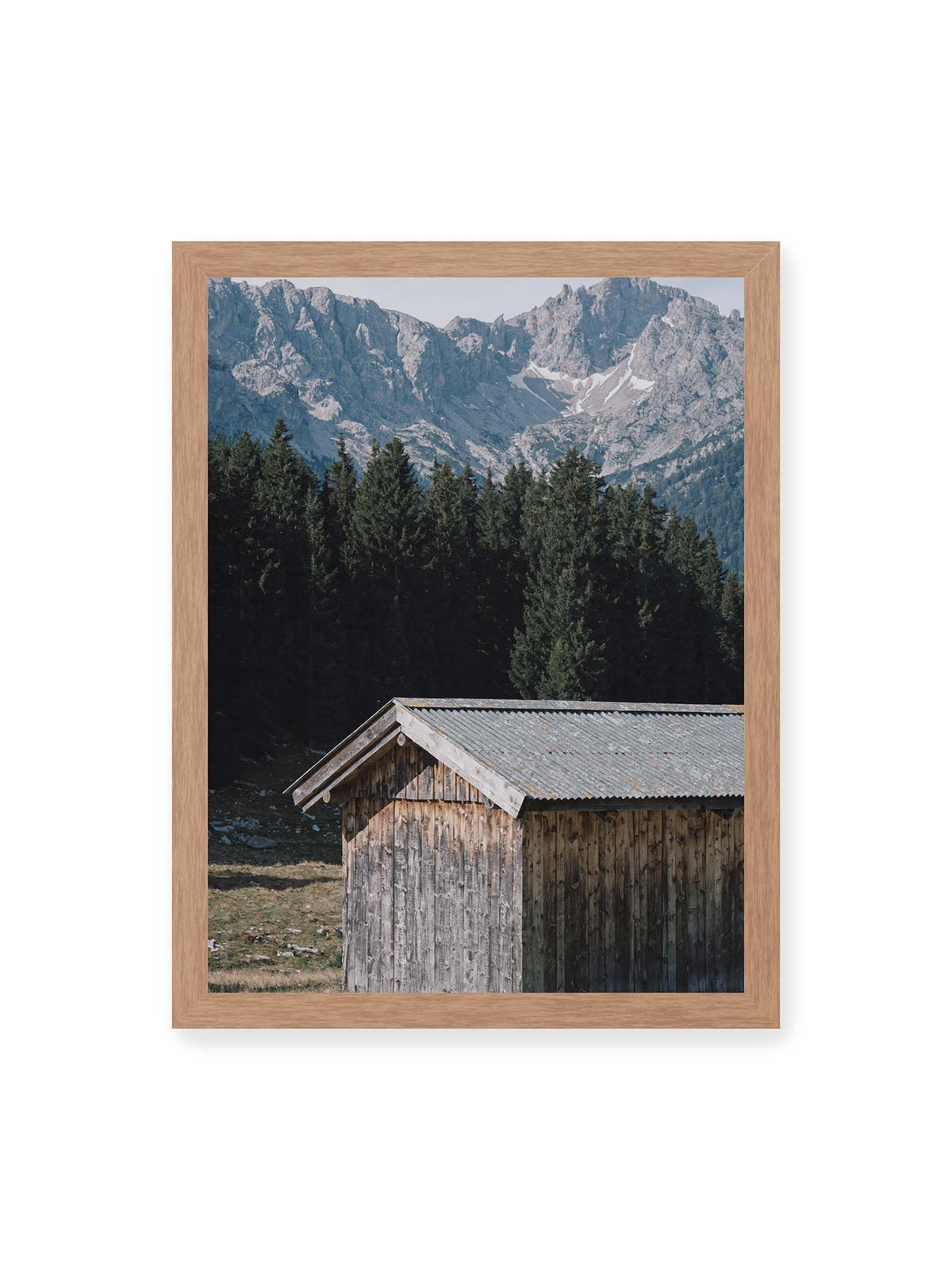 30x40 cm, Eichenrahmen – Verwitterte Holzhütte vor dunklen Nadelbäumen und einer hellen, zerklüfteten Bergkulisse.