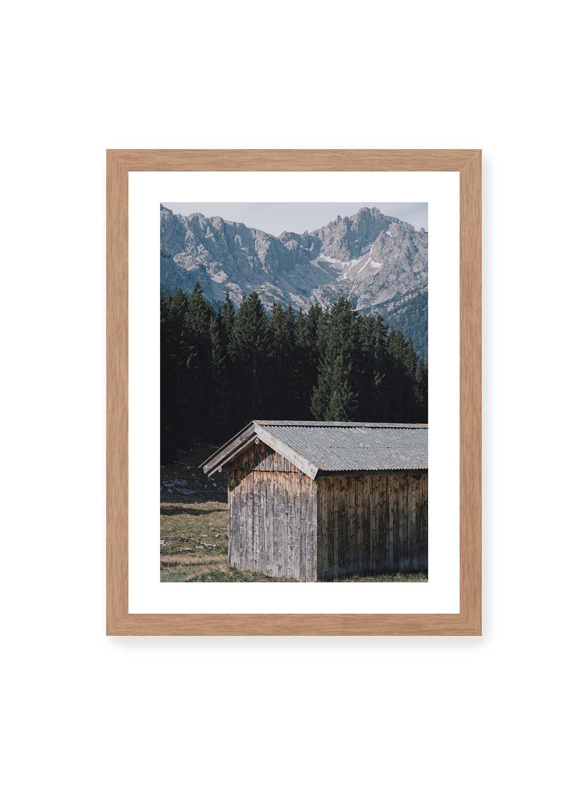 30x40 cm, weißer Galerie-Rand, Eichenrahmen – Verwitterte Holzhütte vor dunklen Nadelbäumen und einer hellen, zerklüfteten Bergkulisse.
