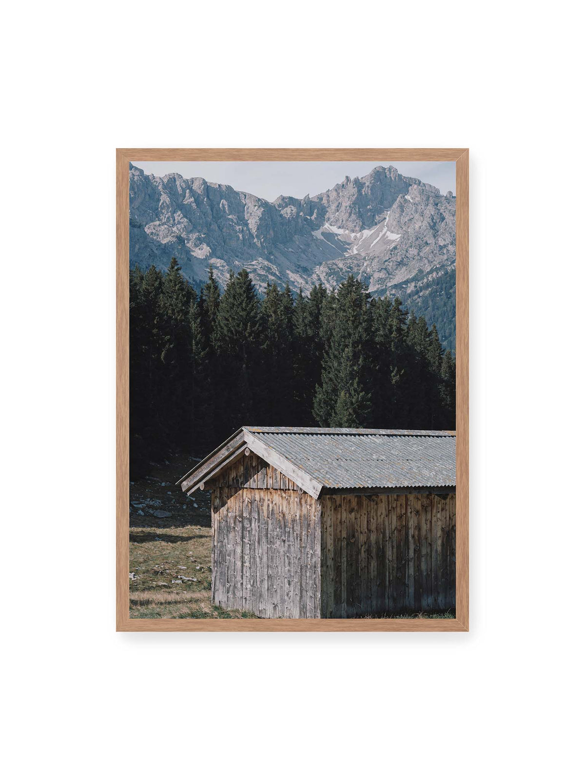 50x70 cm, Eichenrahmen – Verwitterte Holzhütte vor dunklen Nadelbäumen und einer hellen, zerklüfteten Bergkulisse.