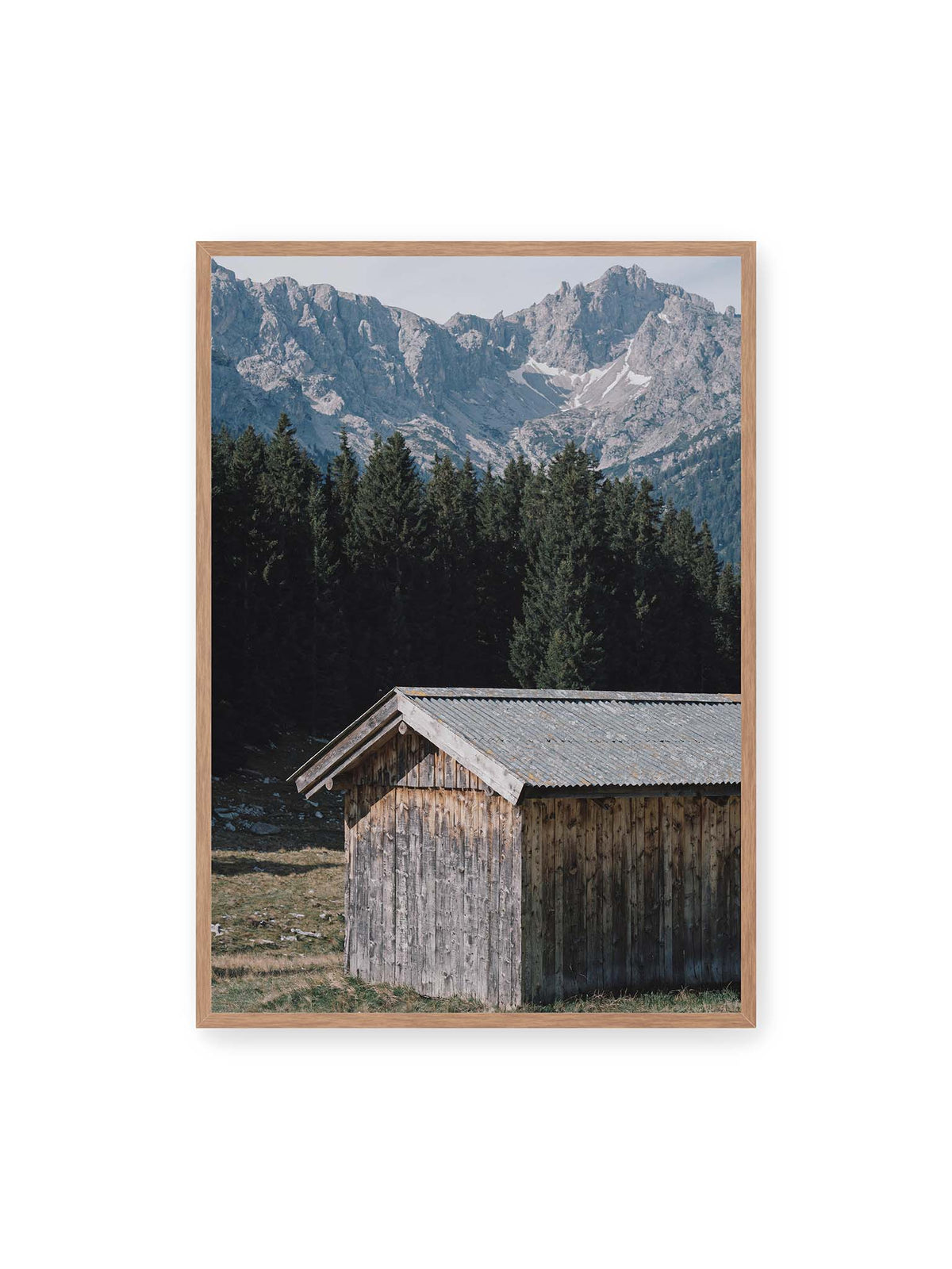70x100 cm, Eichenrahmen – Verwitterte Holzhütte vor dunklen Nadelbäumen und einer hellen, zerklüfteten Bergkulisse.