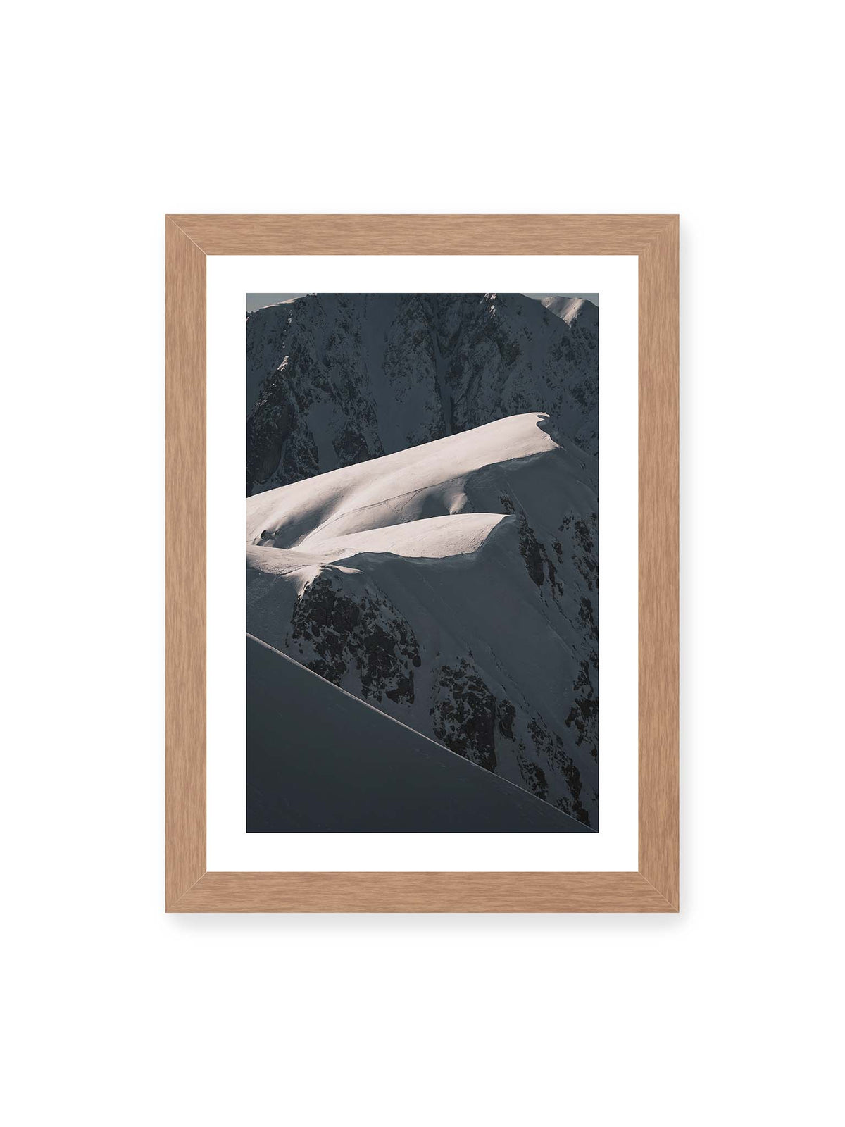 21x30 cm, weißer Galerie-Rand, Eichenrahmen – Verschneite Bergrücken mit hellen Graten und tiefen Schatten vor einer dunklen, steilen Felskulisse.
