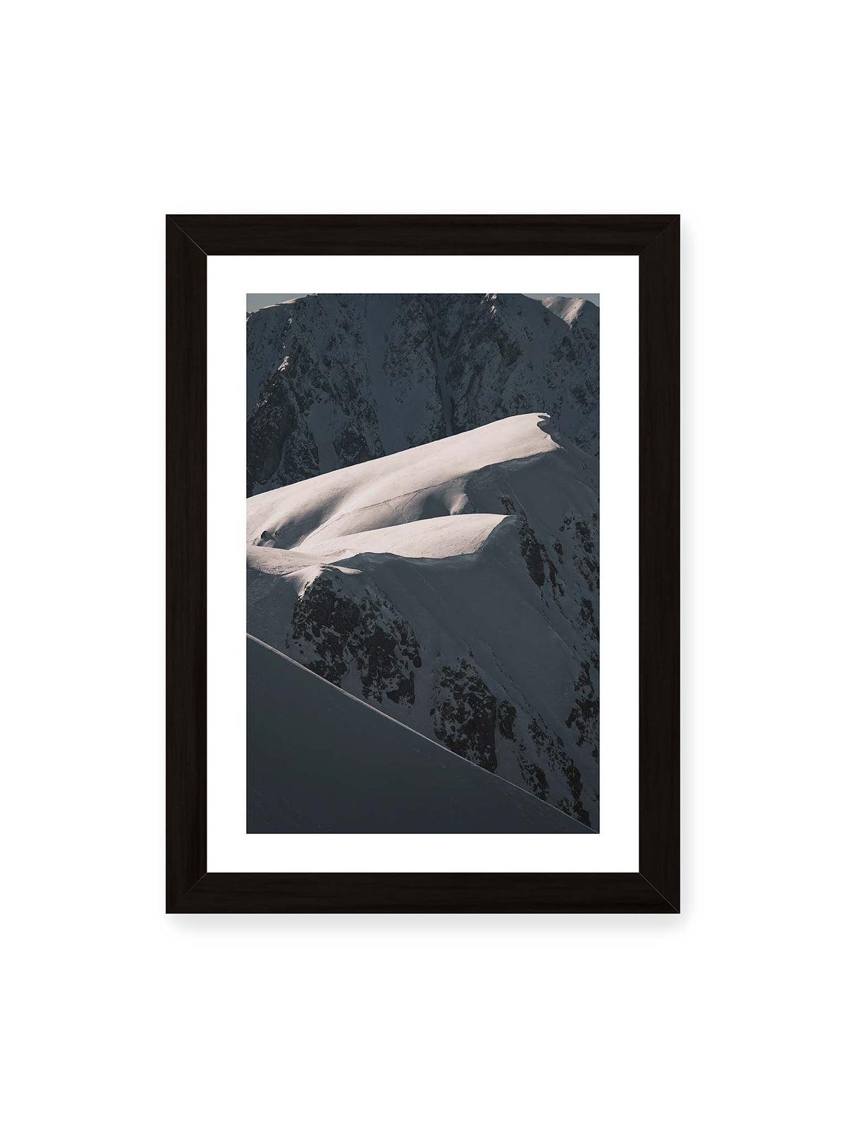 21x30 cm, weißer Galerie-Rand, schwarzer Rahmen – Verschneite Bergrücken mit hellen Graten und tiefen Schatten vor einer dunklen, steilen Felskulisse.