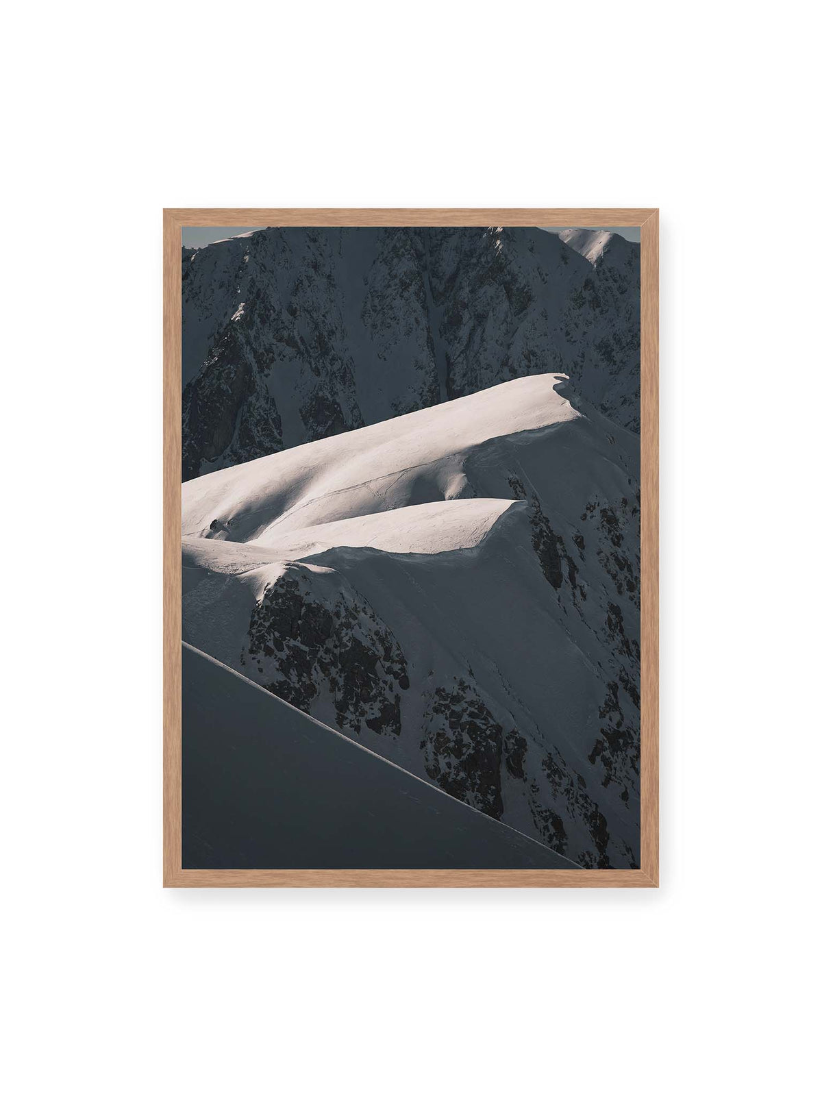 50x70 cm, Eichenrahmen – Verschneite Bergrücken mit hellen Graten und tiefen Schatten vor einer dunklen, steilen Felskulisse.
