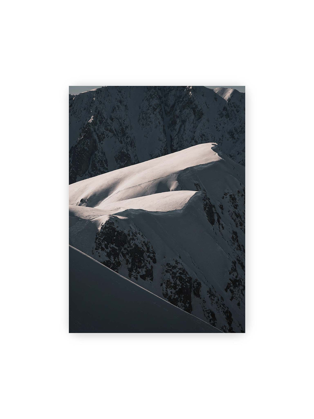 50x70 cm – Verschneite Bergrücken mit hellen Graten und tiefen Schatten vor einer dunklen, steilen Felskulisse.