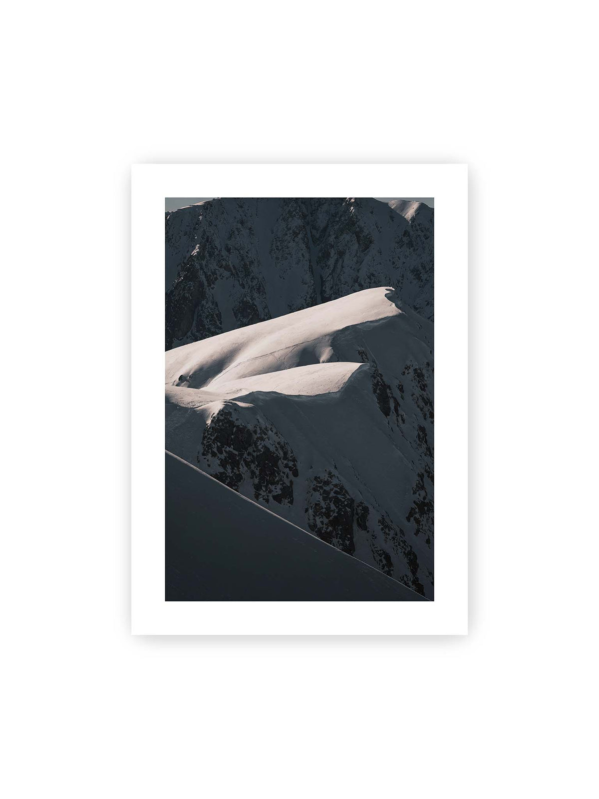 50x70 cm, weißer Galerie-Rand – Verschneite Bergrücken mit hellen Graten und tiefen Schatten vor einer dunklen, steilen Felskulisse.