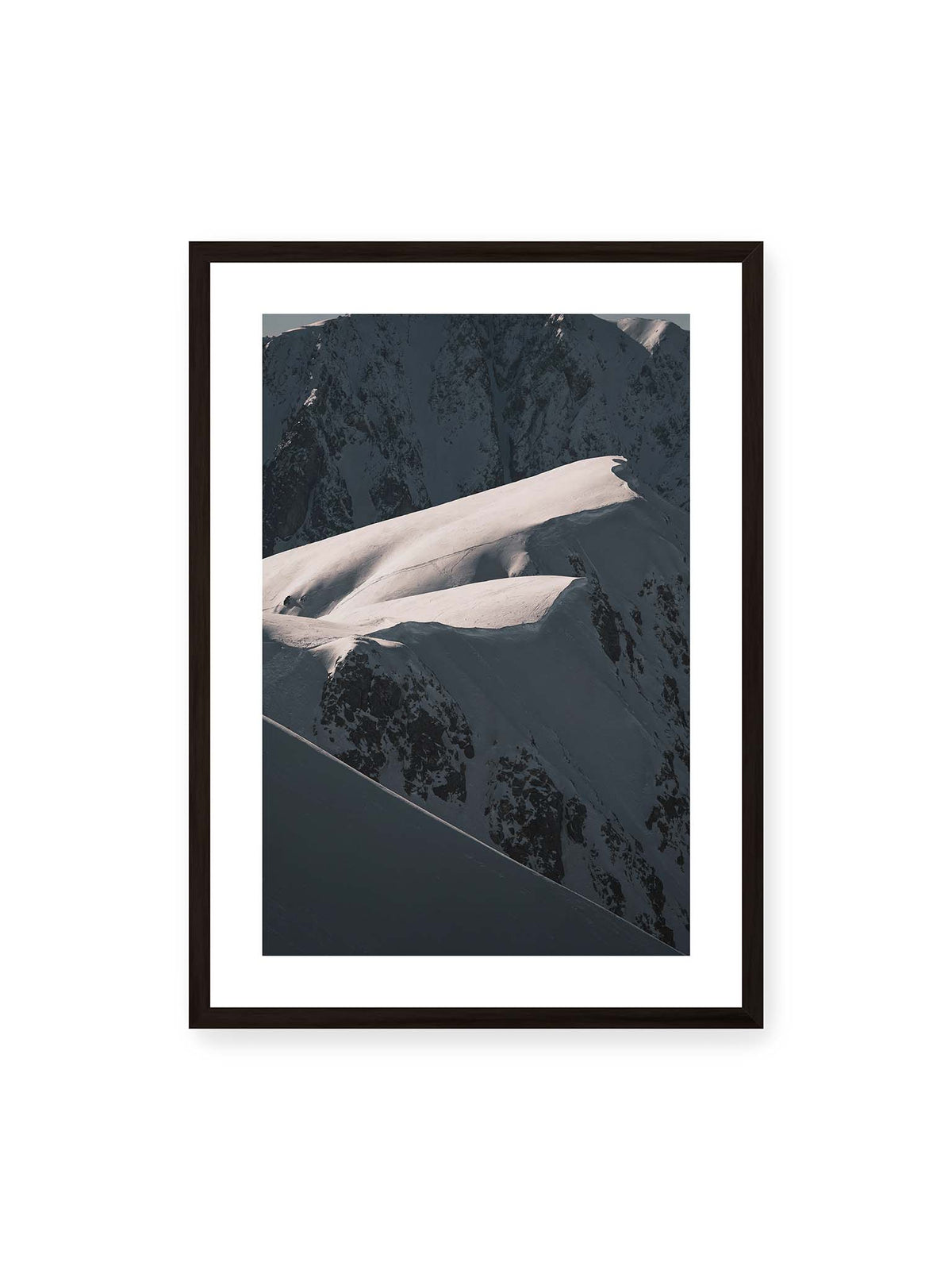 50x70 cm, weißer Galerie-Rand, schwarzer Rahmen – Verschneite Bergrücken mit hellen Graten und tiefen Schatten vor einer dunklen, steilen Felskulisse.