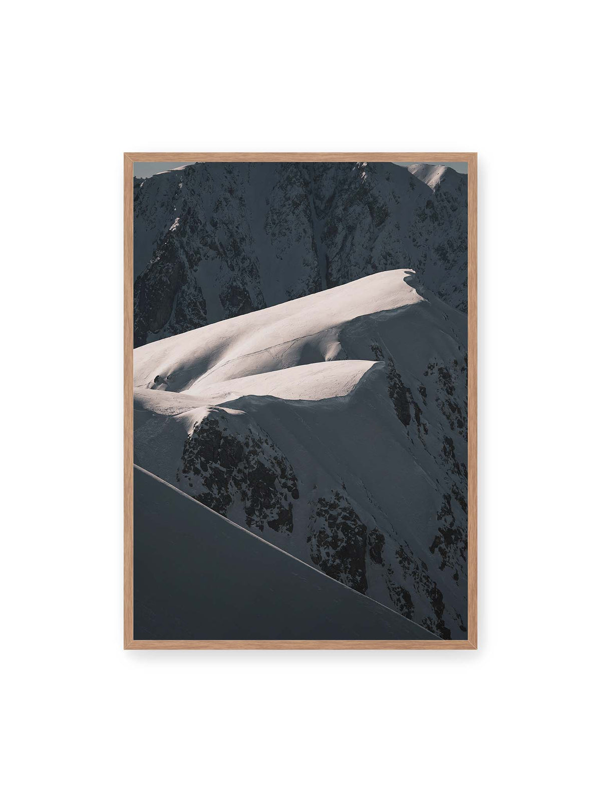 70x100 cm, Eichenrahmen – Verschneite Bergrücken mit hellen Graten und tiefen Schatten vor einer dunklen, steilen Felskulisse.