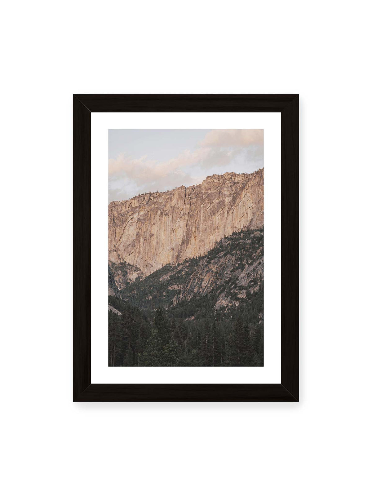 21x30 cm, weißer Galerie-Rand, schwarzer Rahmen – Helle, zerklüftete Felswand über dichtem Nadelwald und dunklen bewaldeten Berghängen.