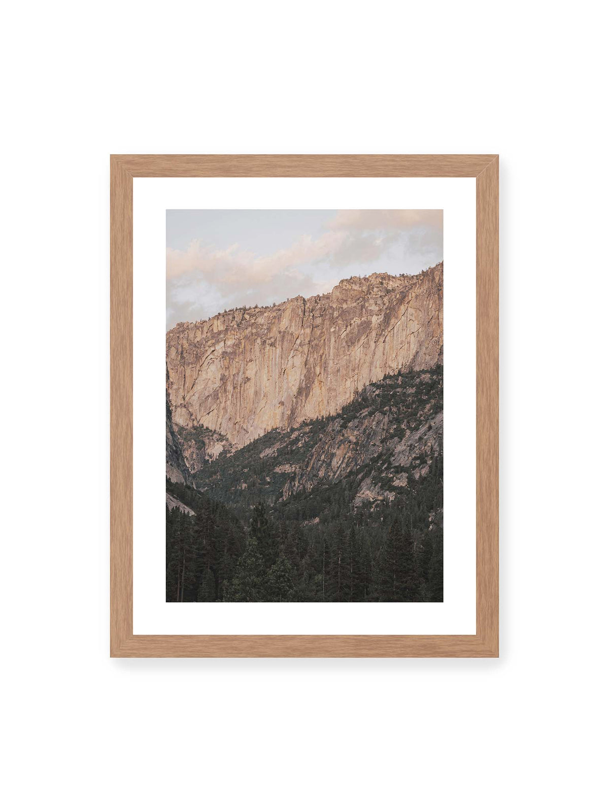 30x40 cm, weißer Galerie-Rand, Eichenrahmen – Helle, zerklüftete Felswand über dichtem Nadelwald und dunklen bewaldeten Berghängen.