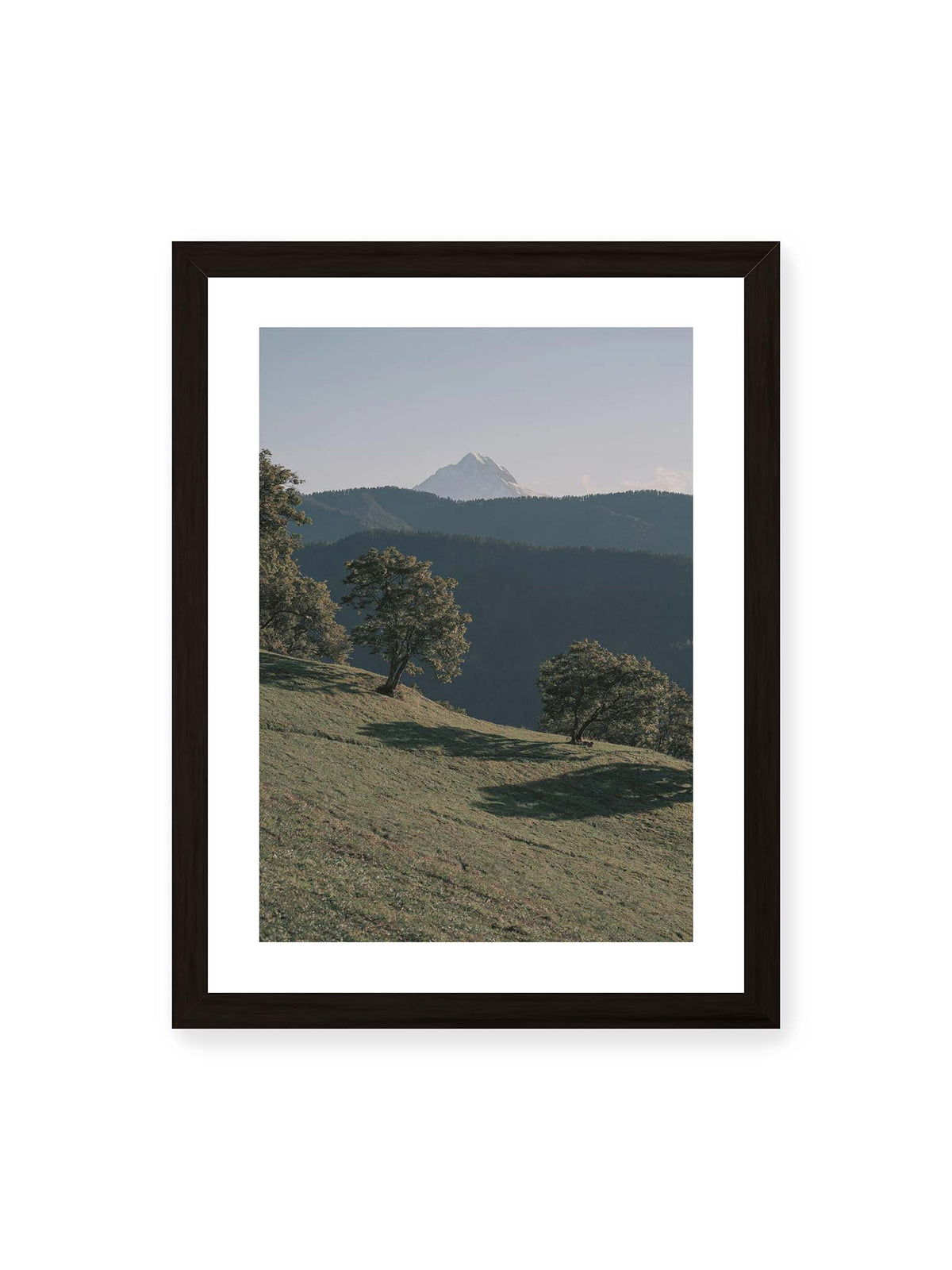 30x40 cm, weißer Galerie-Rand, schwarzer Rahmen – Ferner heller Berggipfel über dunklen Höhenzügen und einer geneigten grünen Wiese mit einzelnen Bäumen.