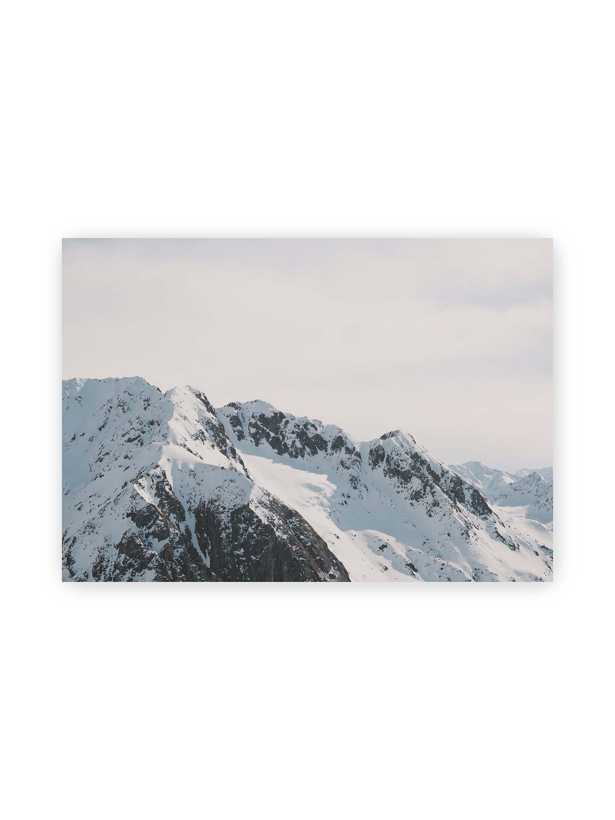 100x70 cm – Verschneite Bergkette mit schroffen Felswänden und gestaffelten Gipfeln unter einem hellen, weiten Himmel.