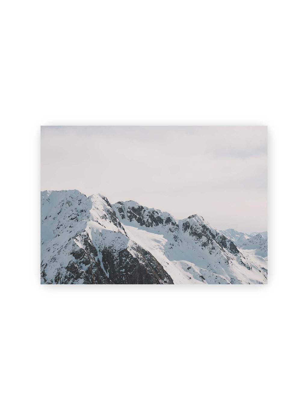 30x21 cm – Verschneite Bergkette mit schroffen Felswänden und gestaffelten Gipfeln unter einem hellen, weiten Himmel.