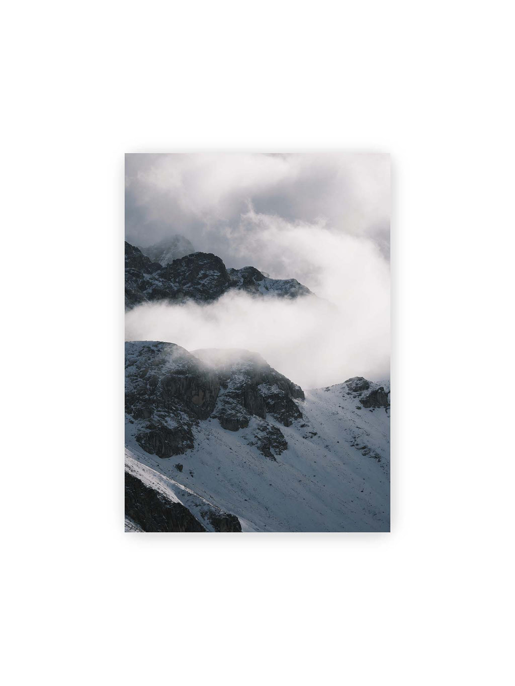 21x30 cm – Verschneite dunkle Felsrücken ragen zwischen dichten, tief ziehenden Wolken hervor.