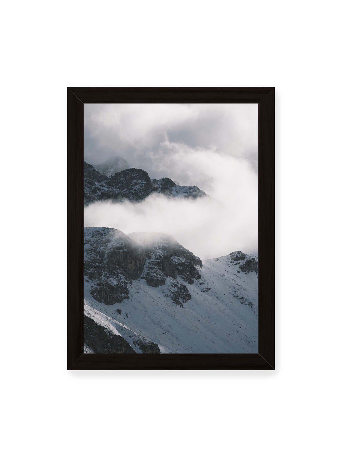 21x30 cm, schwarzer Rahmen – Verschneite dunkle Felsrücken ragen zwischen dichten, tief ziehenden Wolken hervor.