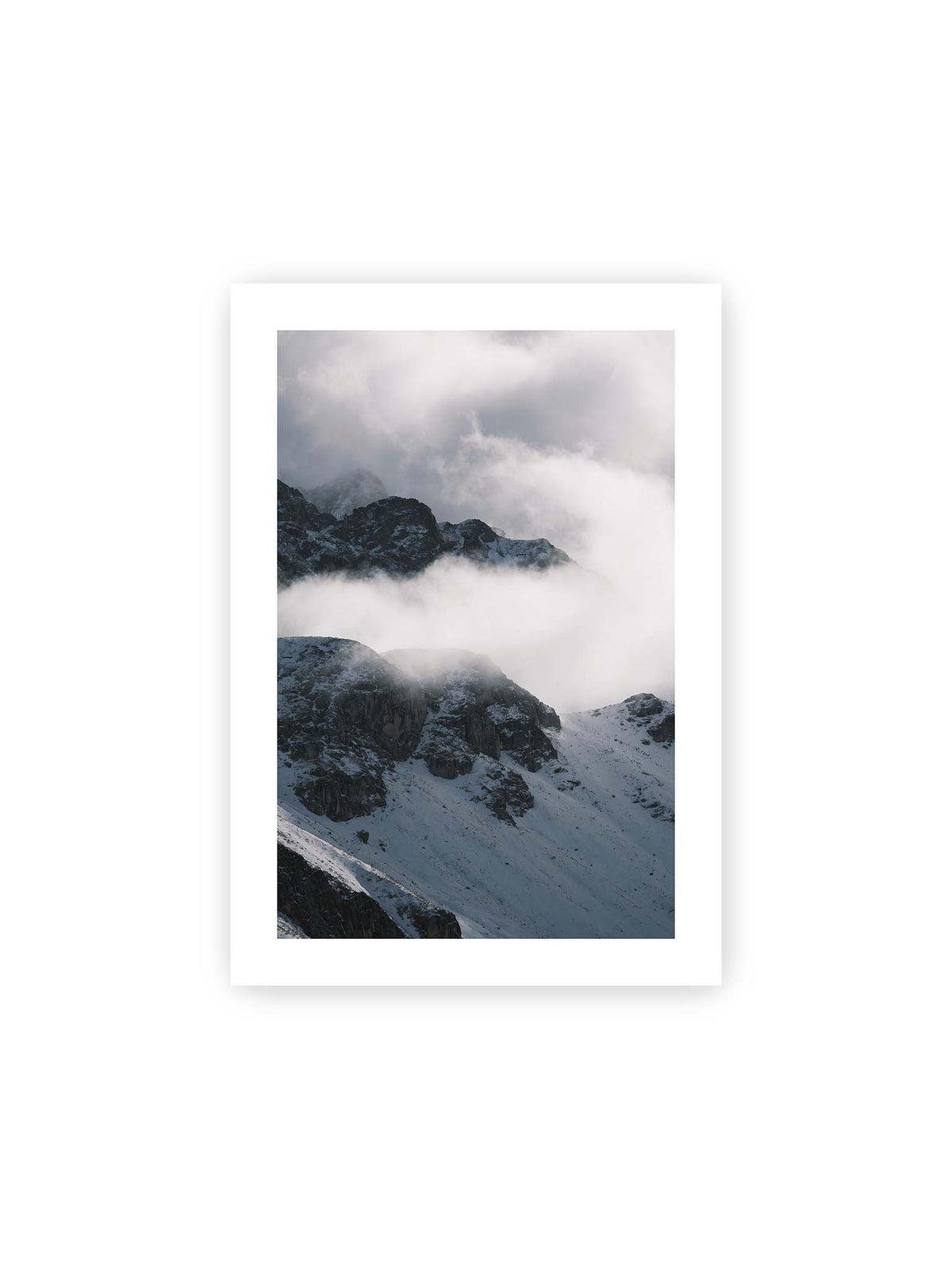 21x30 cm, weißer Galerie-Rand – Verschneite dunkle Felsrücken ragen zwischen dichten, tief ziehenden Wolken hervor.