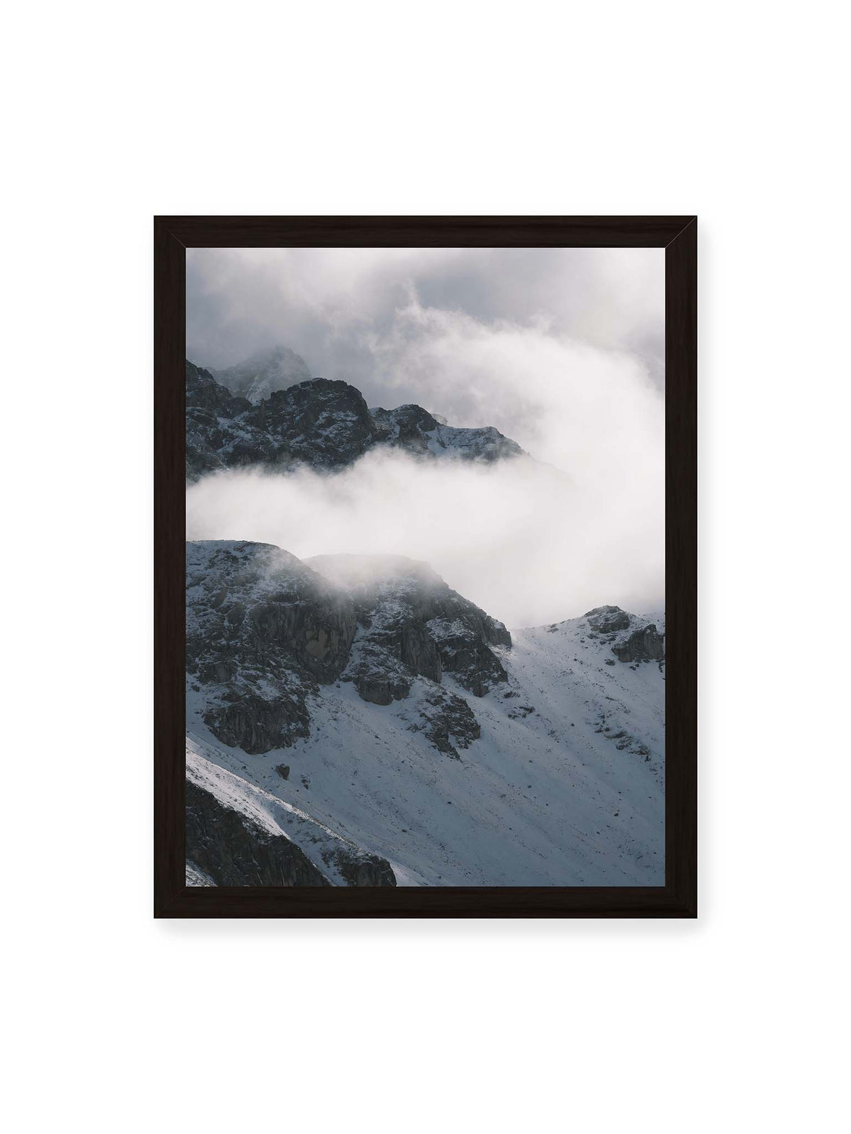 30x40 cm, schwarzer Rahmen – Verschneite dunkle Felsrücken ragen zwischen dichten, tief ziehenden Wolken hervor.