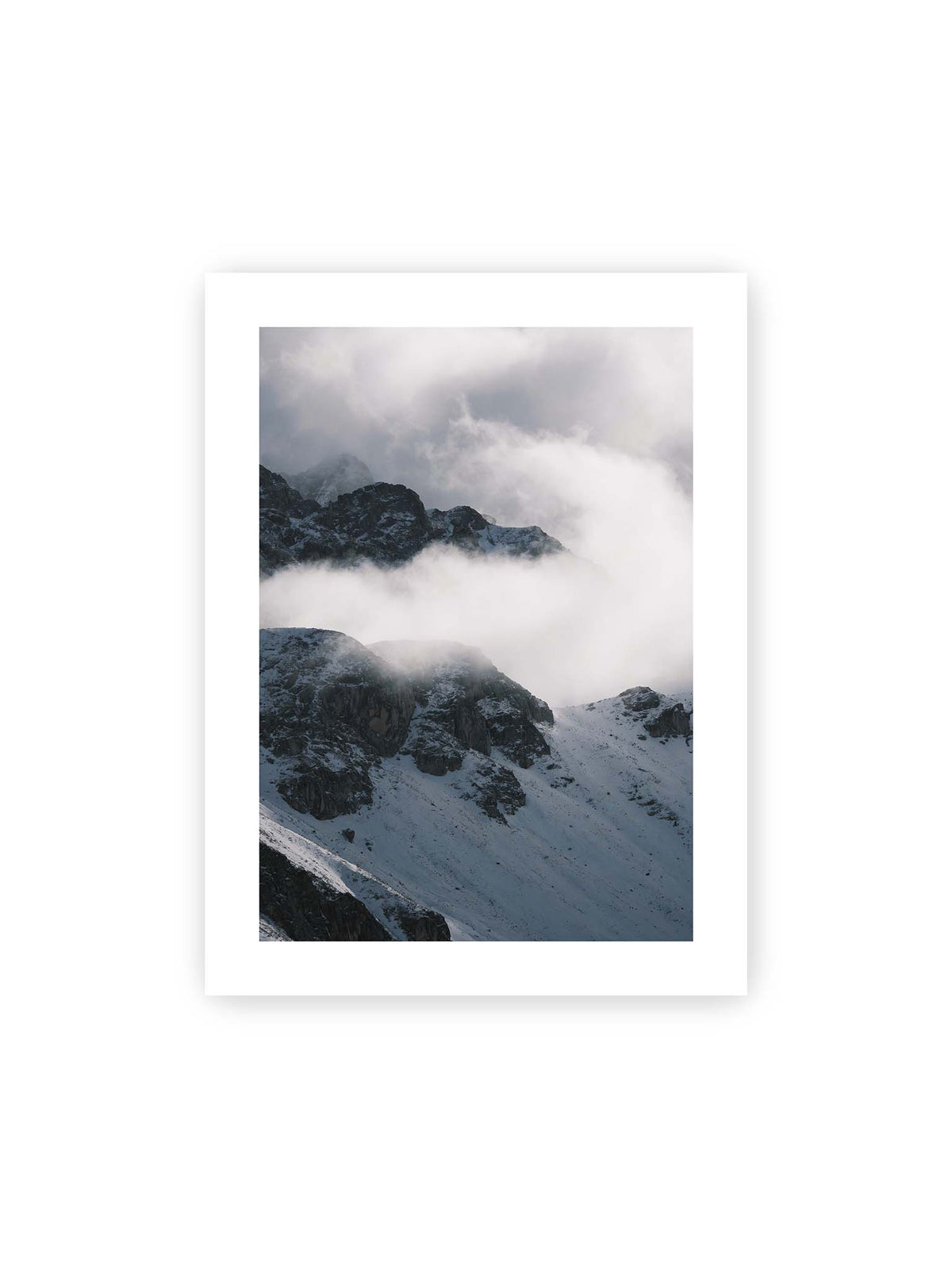 30x40 cm, weißer Galerie-Rand – Verschneite dunkle Felsrücken ragen zwischen dichten, tief ziehenden Wolken hervor.