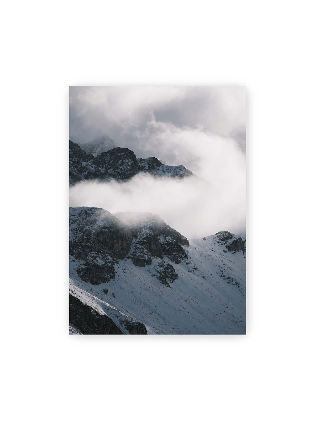 50x70 cm – Verschneite dunkle Felsrücken ragen zwischen dichten, tief ziehenden Wolken hervor.