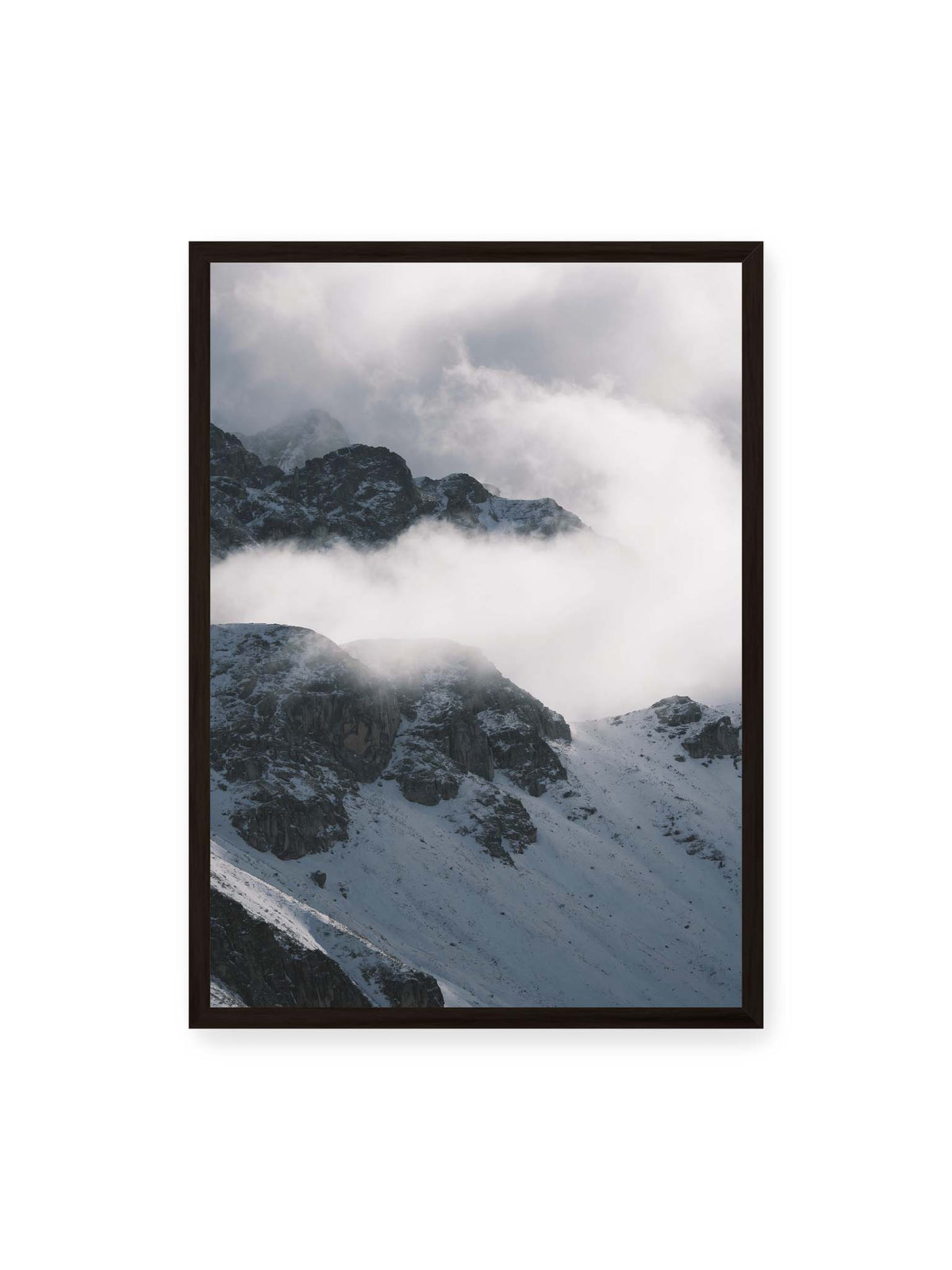 50x70 cm, schwarzer Rahmen – Verschneite dunkle Felsrücken ragen zwischen dichten, tief ziehenden Wolken hervor.