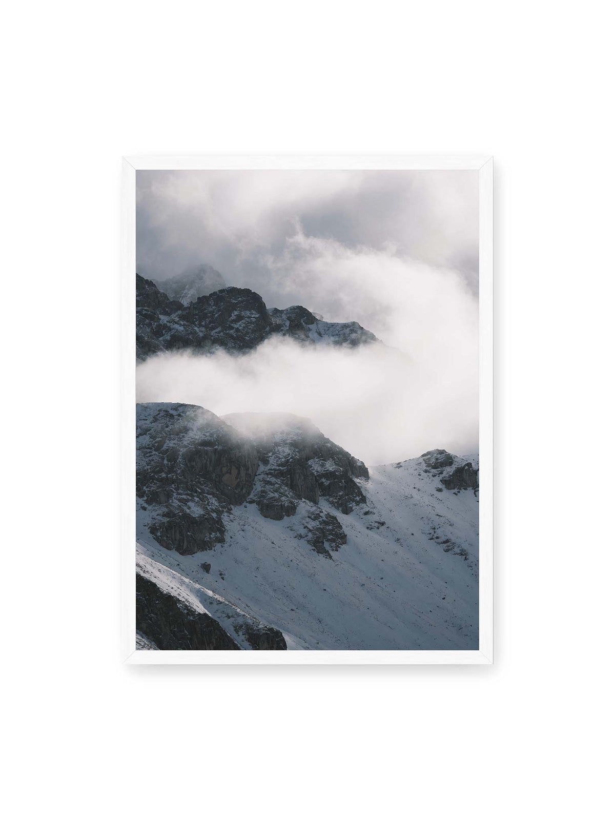 50x70 cm, weißer Rahmen – Verschneite dunkle Felsrücken ragen zwischen dichten, tief ziehenden Wolken hervor.