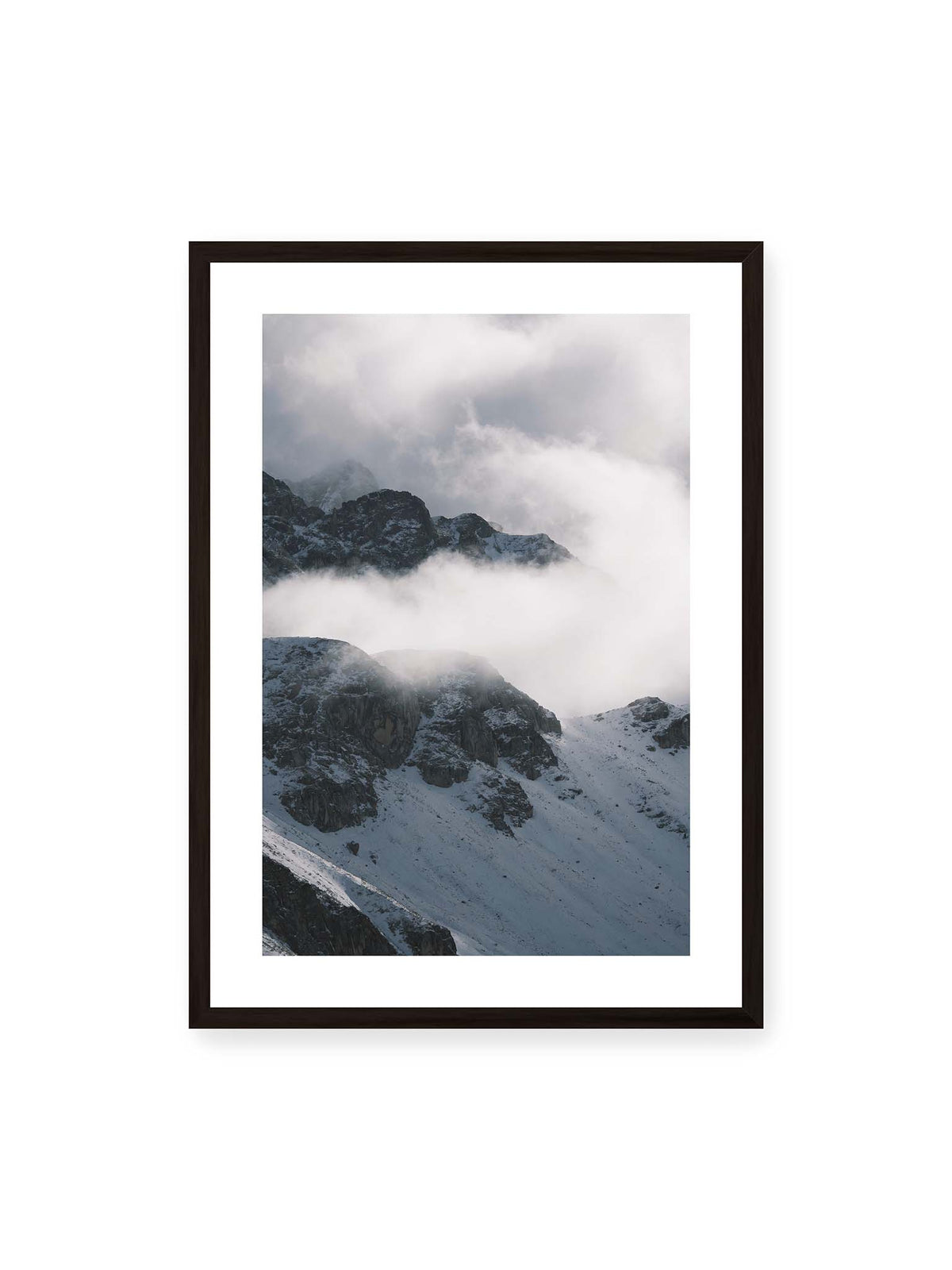 50x70 cm, weißer Galerie-Rand, schwarzer Rahmen – Verschneite dunkle Felsrücken ragen zwischen dichten, tief ziehenden Wolken hervor.