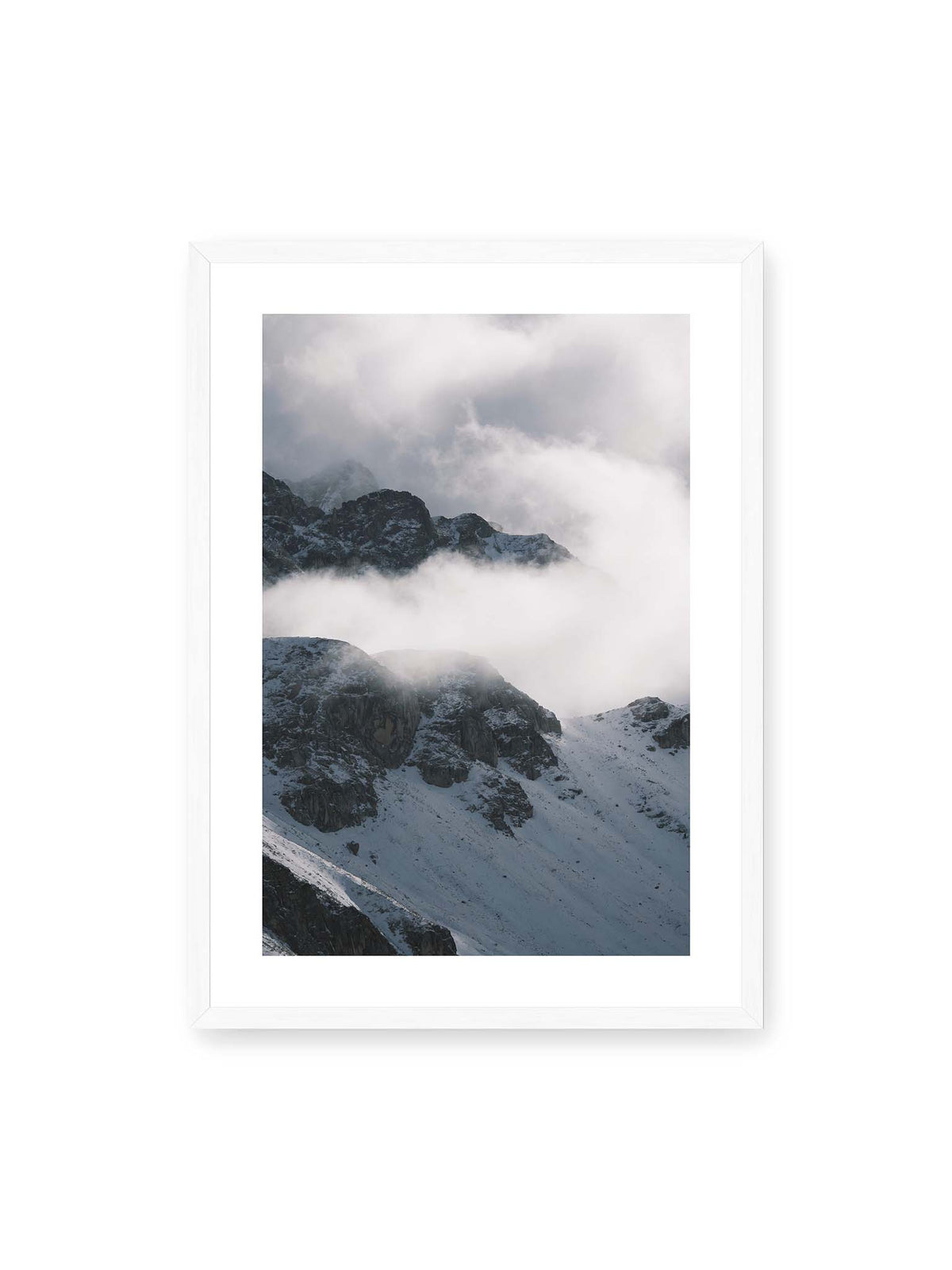 50x70 cm, weißer Galerie-Rand, weißer Rahmen – Verschneite dunkle Felsrücken ragen zwischen dichten, tief ziehenden Wolken hervor.