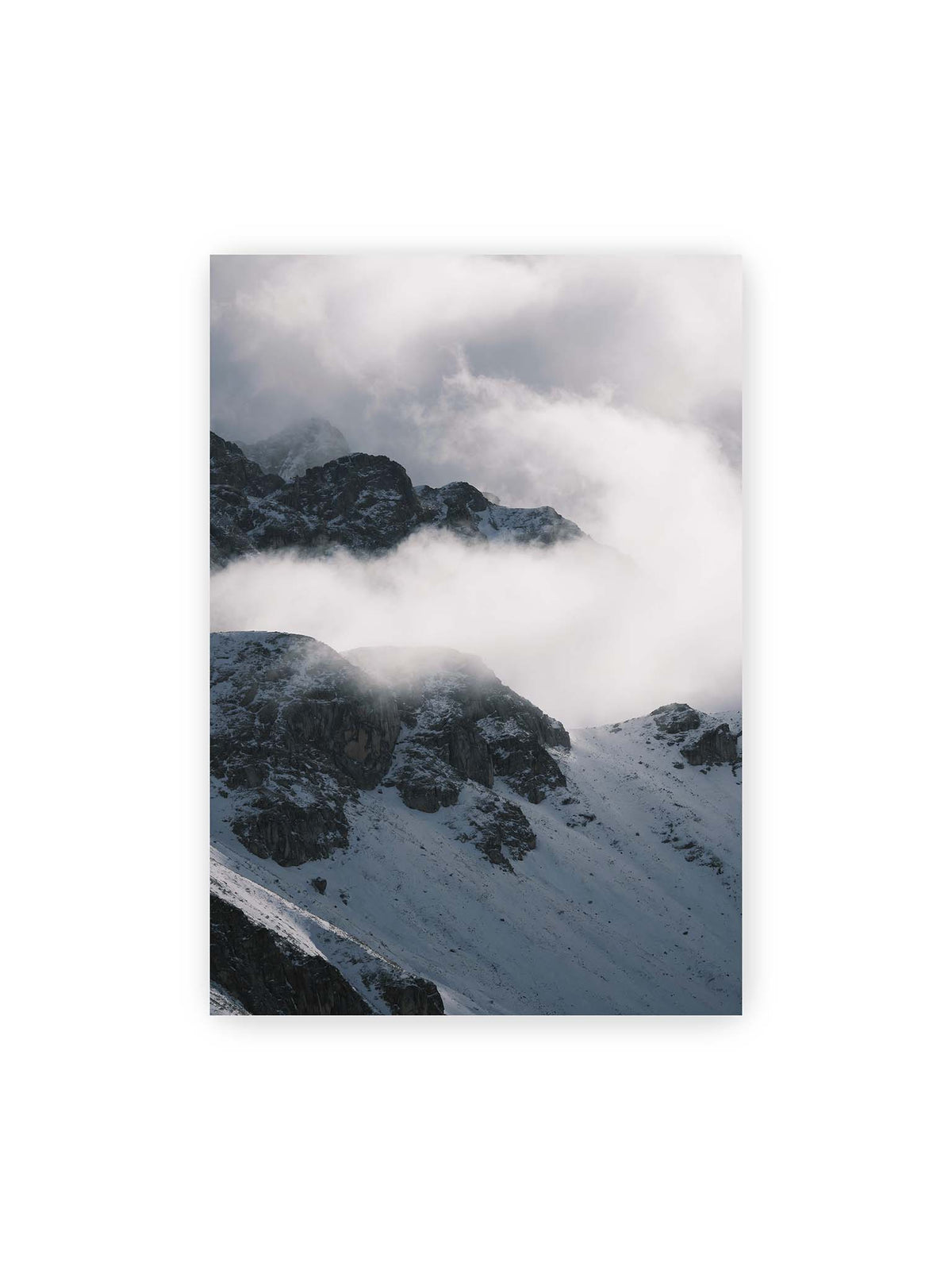 70x100 cm – Verschneite dunkle Felsrücken ragen zwischen dichten, tief ziehenden Wolken hervor.
