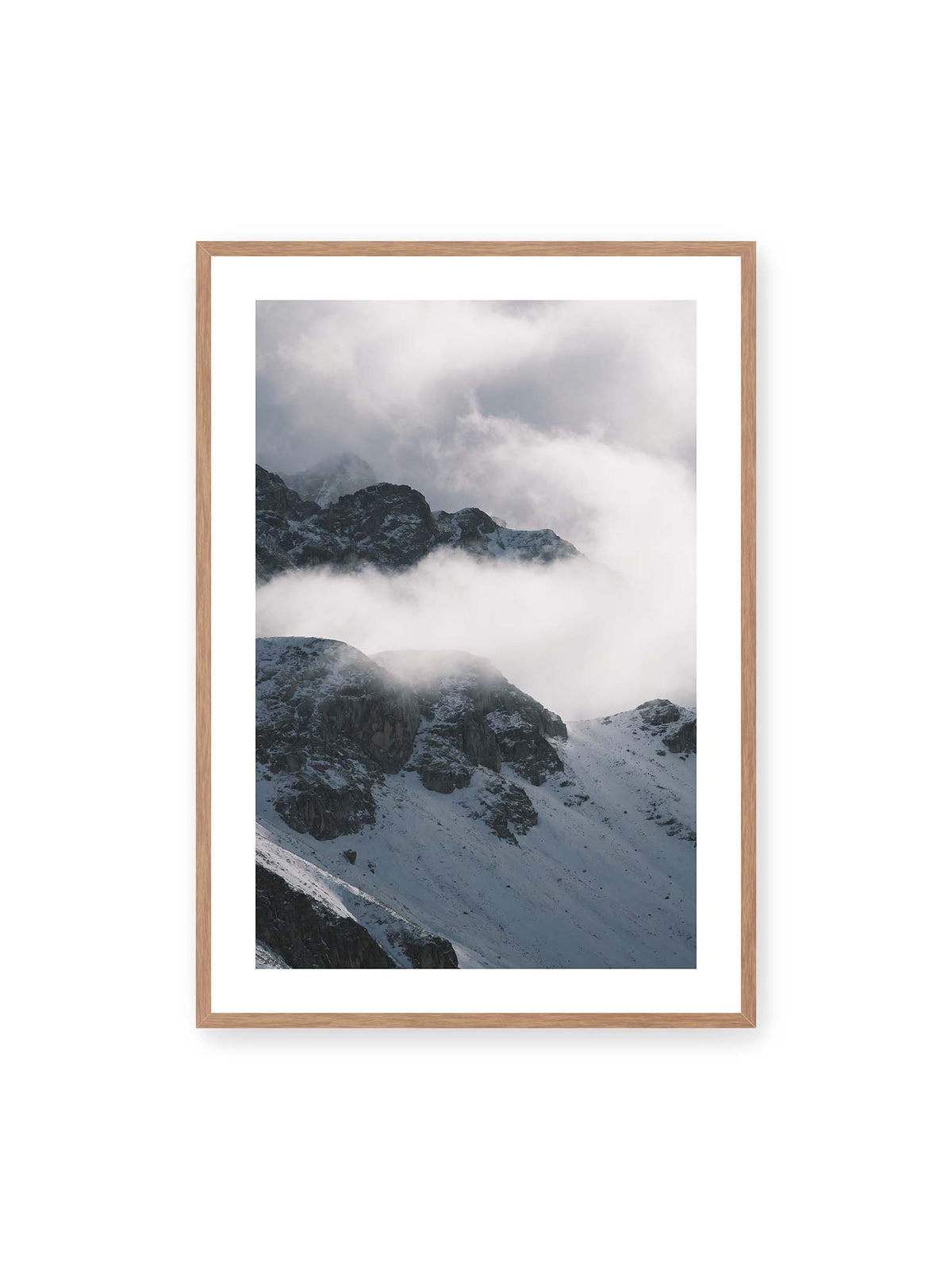 70x100 cm, weißer Galerie-Rand, Eichenrahmen – Verschneite dunkle Felsrücken ragen zwischen dichten, tief ziehenden Wolken hervor.