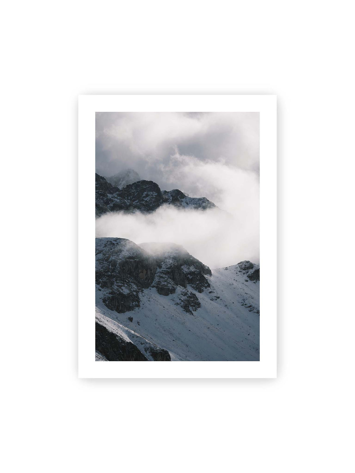 70x100 cm, weißer Galerie-Rand – Verschneite dunkle Felsrücken ragen zwischen dichten, tief ziehenden Wolken hervor.