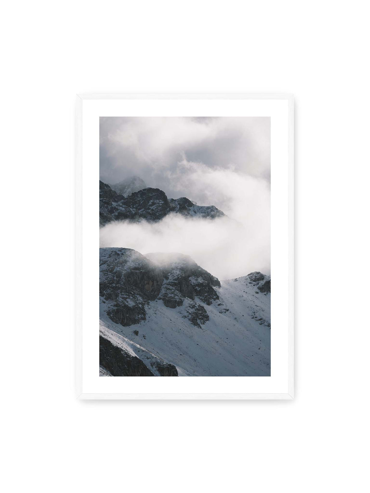 70x100 cm, weißer Galerie-Rand, weißer Rahmen – Verschneite dunkle Felsrücken ragen zwischen dichten, tief ziehenden Wolken hervor.